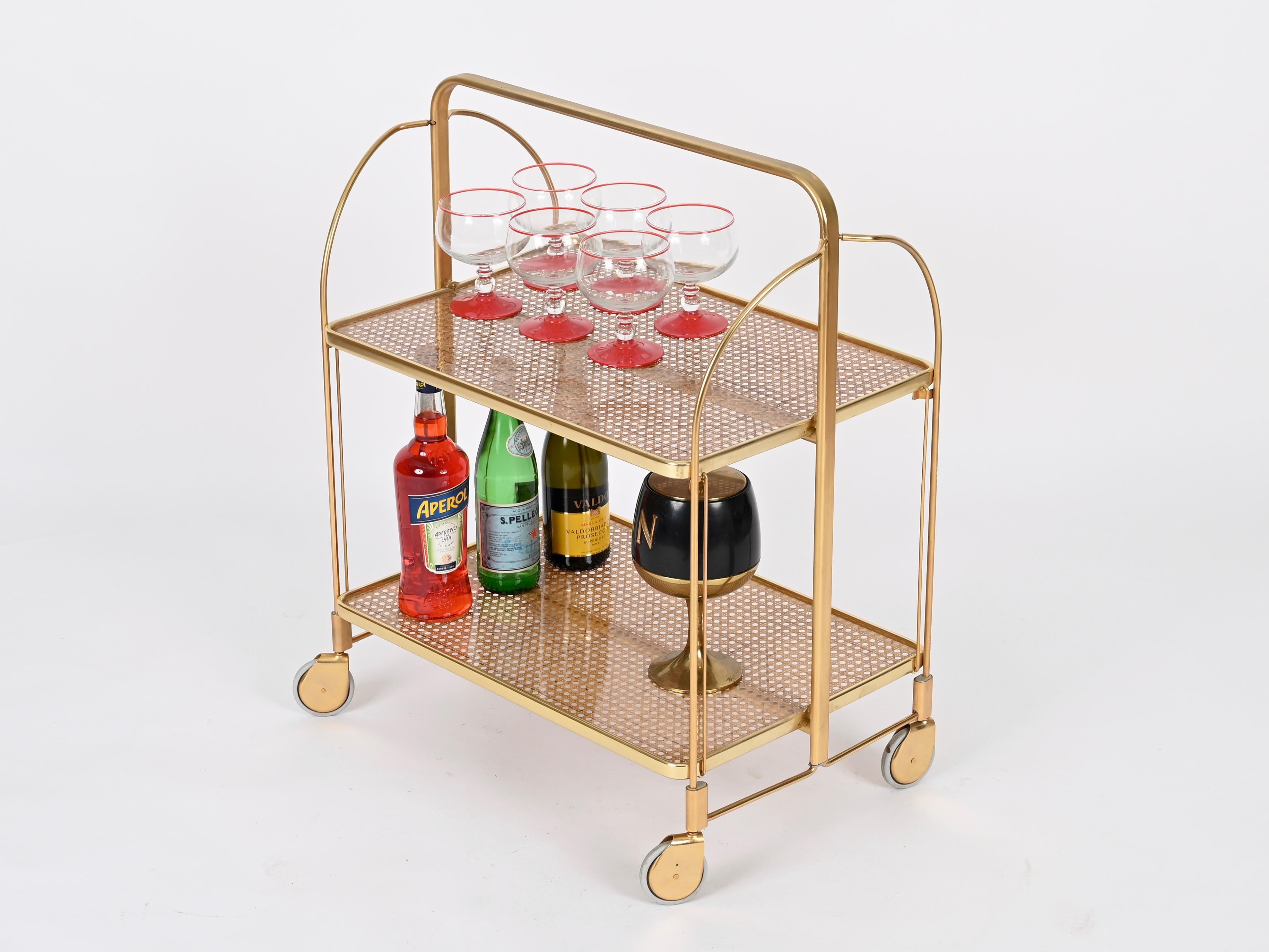 Maravilloso carrito de bar plegable de mediados de siglo para servir, de metal dorado, lucita transparente y paja de Viena. Esta pieza increíblemente elegante y única se fabricó en Italia en la década de 1970 y se atribuye a una producción de Dior