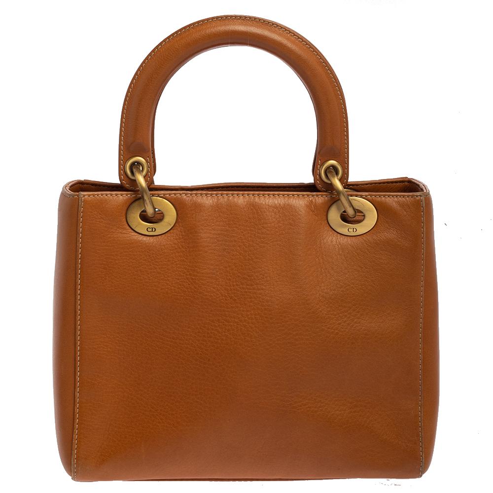 The Lady Dior tote from Dior is a timeless piece. The leather bag comes in a luxurious shade of tan with gold-tone hardware and 'Dior' letter charms. It features dual top handles, a detachable shoulder strap, and protective studs at the bottom. The