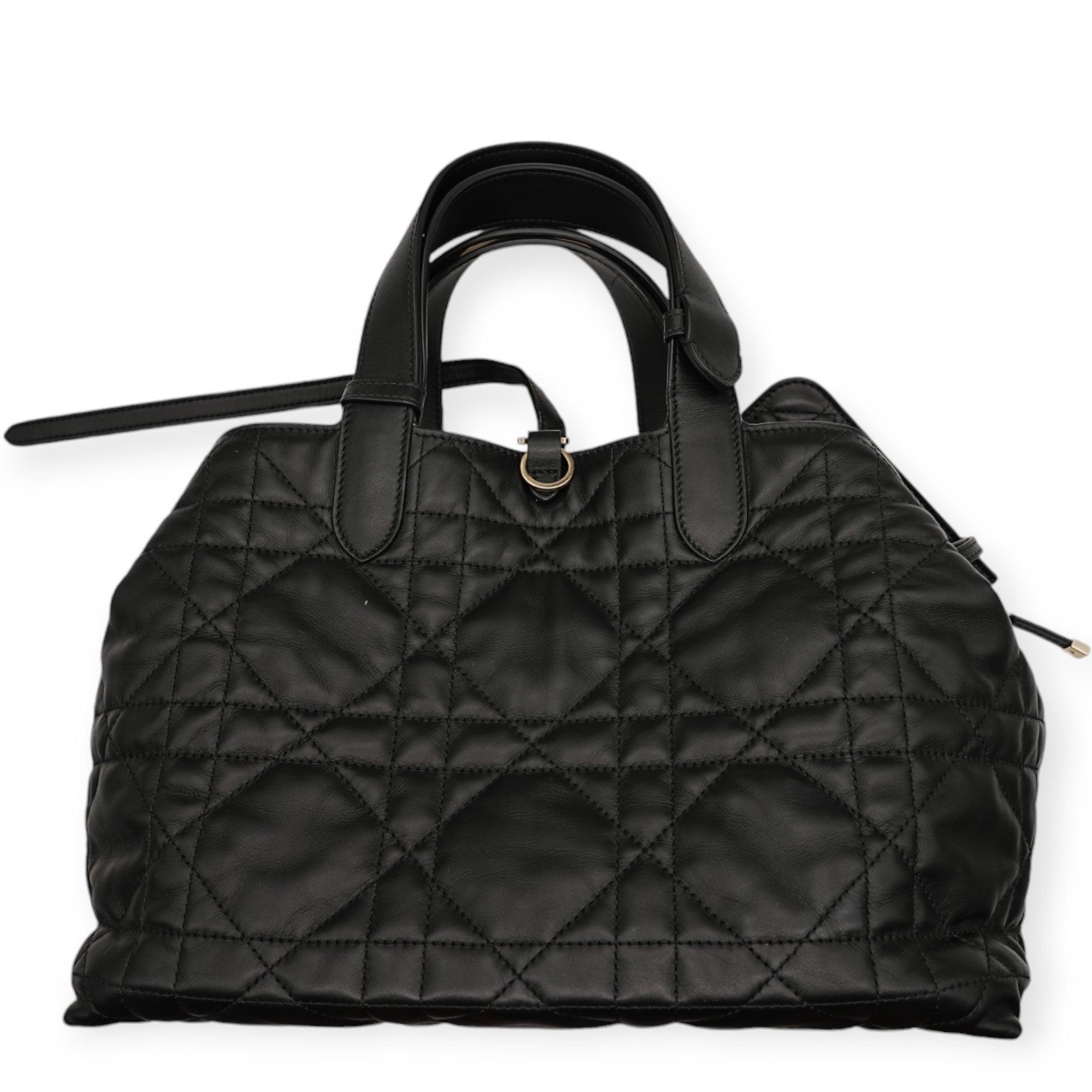 The Dior Toujours handbag is crafted from premium black matte cowhide leather, showcasing luxurious gold hardware accents that enhance its timeless elegance. With a sleek and sophisticated design, this handbag exudes an air of refinement, making it