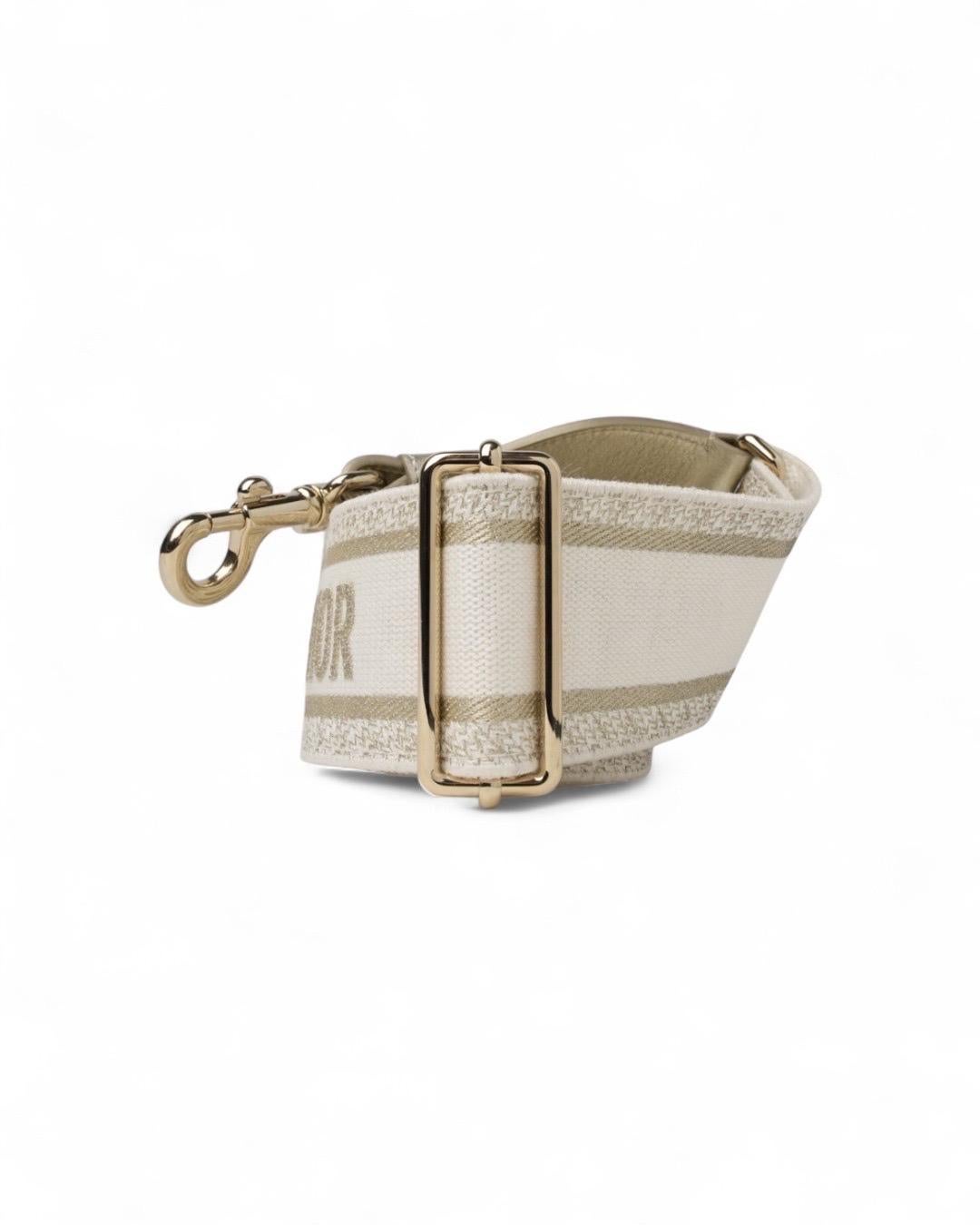 Tracolla firmata Dior, realizzata in elegante tessuto bianco e oro, rifinita con dettagli in pelle e hardware dorati. Questa tracolla è regolabile e rimovibile, offrendo la versatilità necessaria per abbinarla facilmente a qualsiasi borsa. Con un