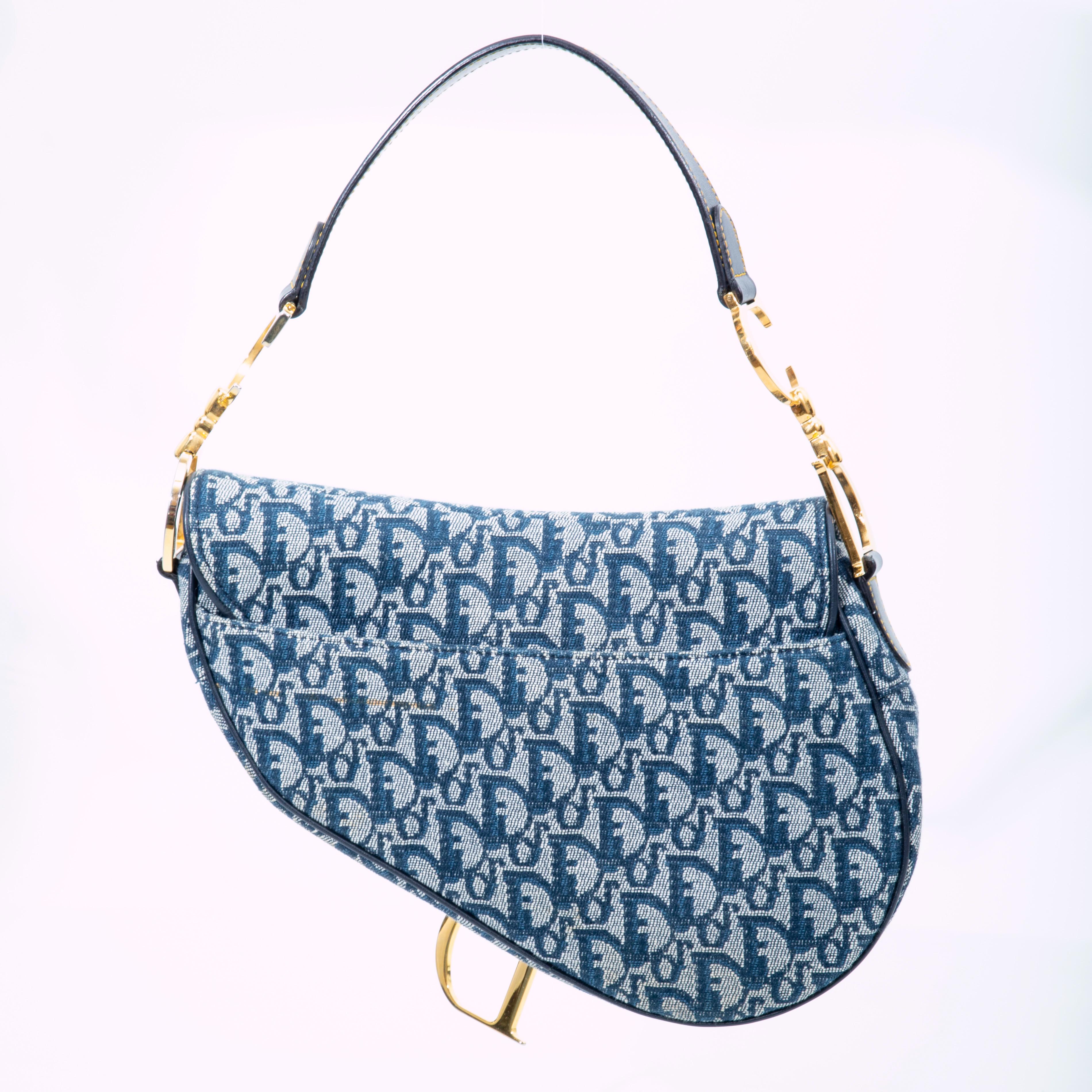 This iconic Dior vintage saddle bag is the original John Galliano design with blue monogram canvas and leather details. The bag features a flat leather shoulder strap, logo charms and links, a fold over flap with a saddle shape, velcro fastening