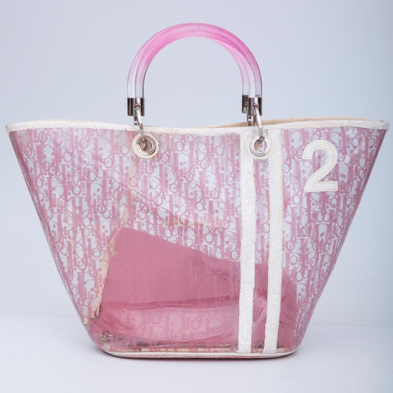 Early 2000’s piece by John Galliano. The bag is made of transparent PVC with pink Diorissimo print throughout and contrasting white leather details and trim. The bag features the number 2 embellished on the front in white leather, dual pink ombre
