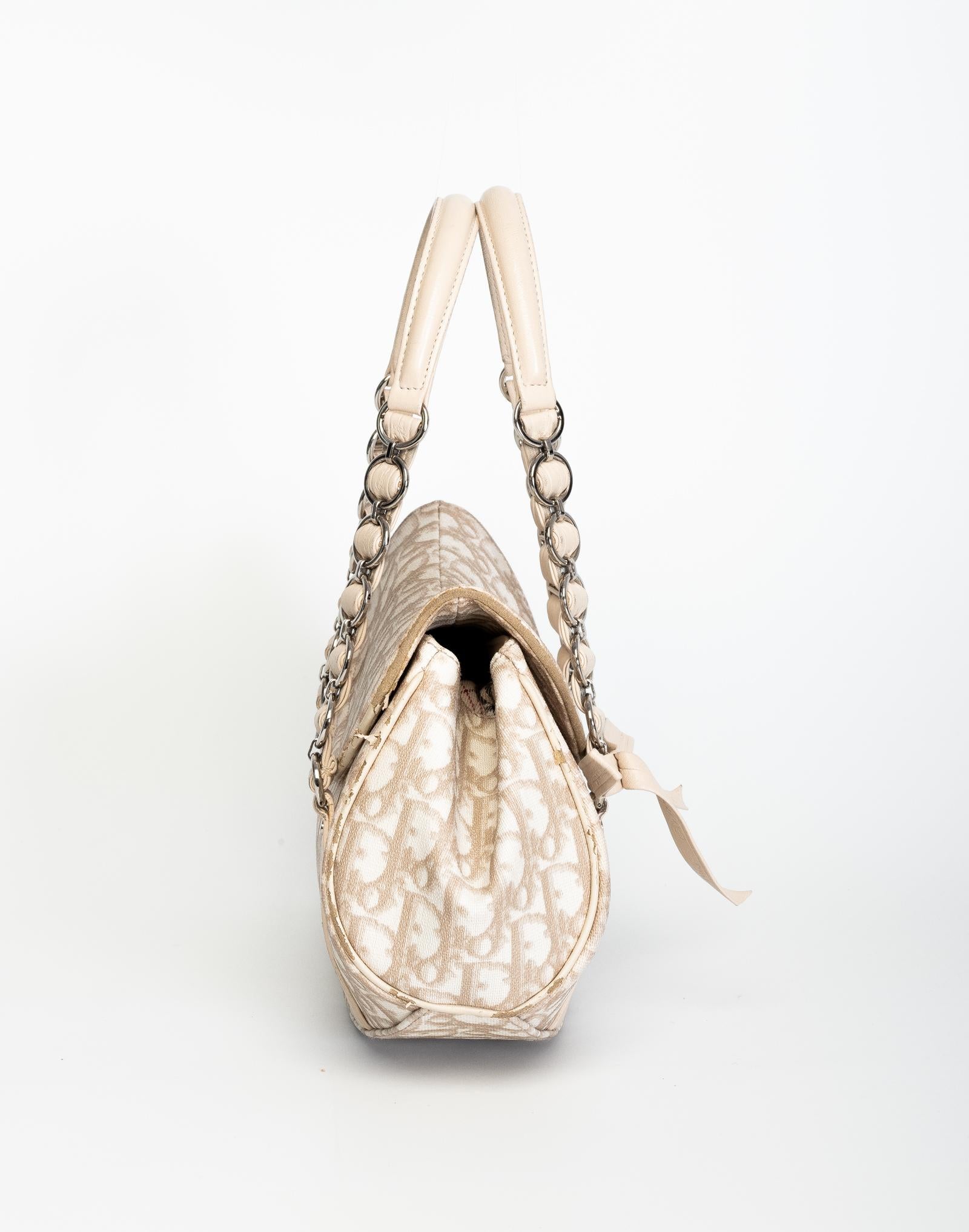 Diese Handtasche von Dior ist aus beschichtetem Canvas mit Lederoberflächen gefertigt und verfügt über das Monogramm von Dior, ein Ledergeflecht mit Metallkette zum Tragen, eine obere Klappe, eine dekorative Schleife auf der Vorderseite und ein
