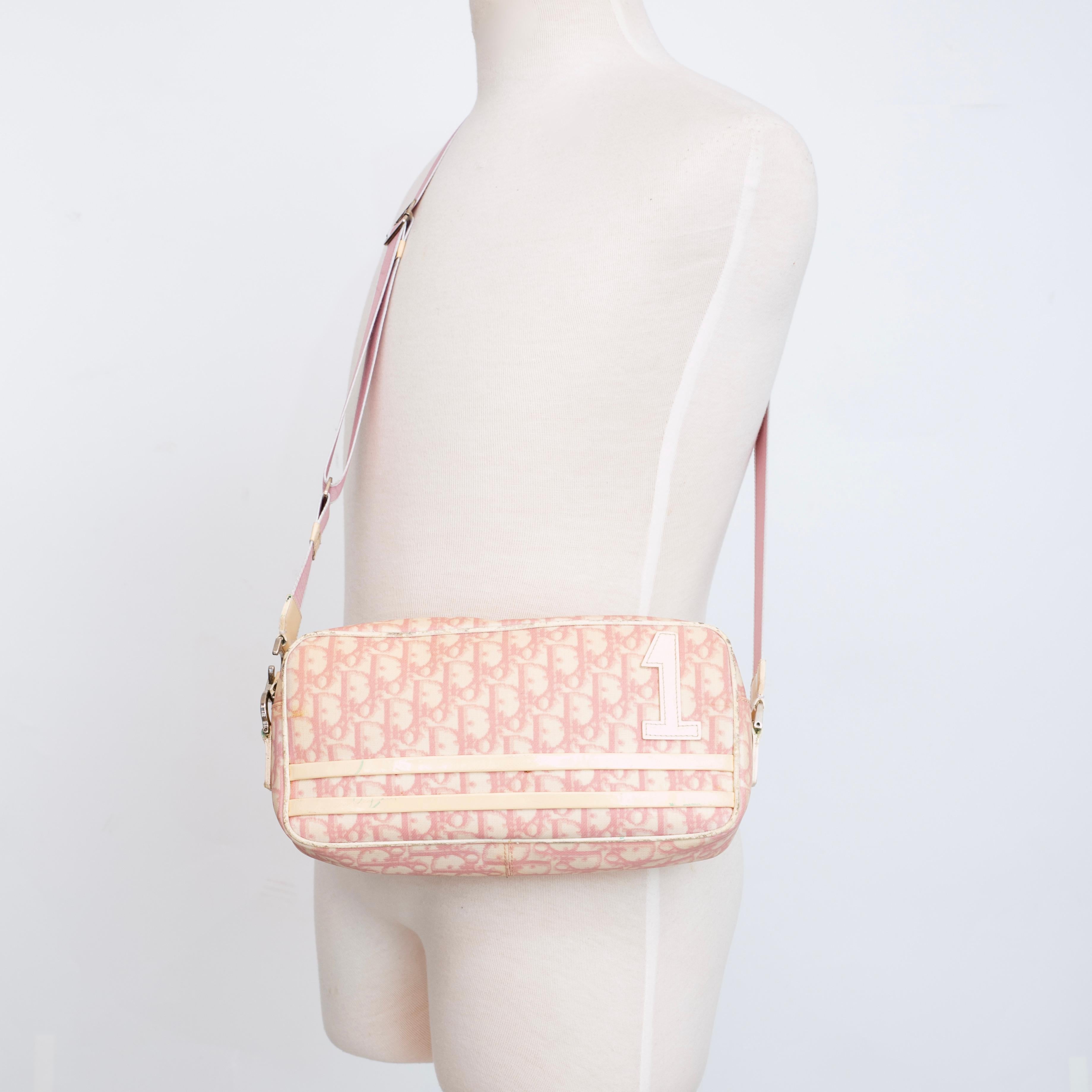 This rectangular shoulder bag is made with white coated canvas with Dior’s oblique monogram print in pink. The bag features studs, a white flower, “number 1” and studs embroidered on the front. Designed by Galliano.

COLOR: Pink monogram
MATERIAL:
