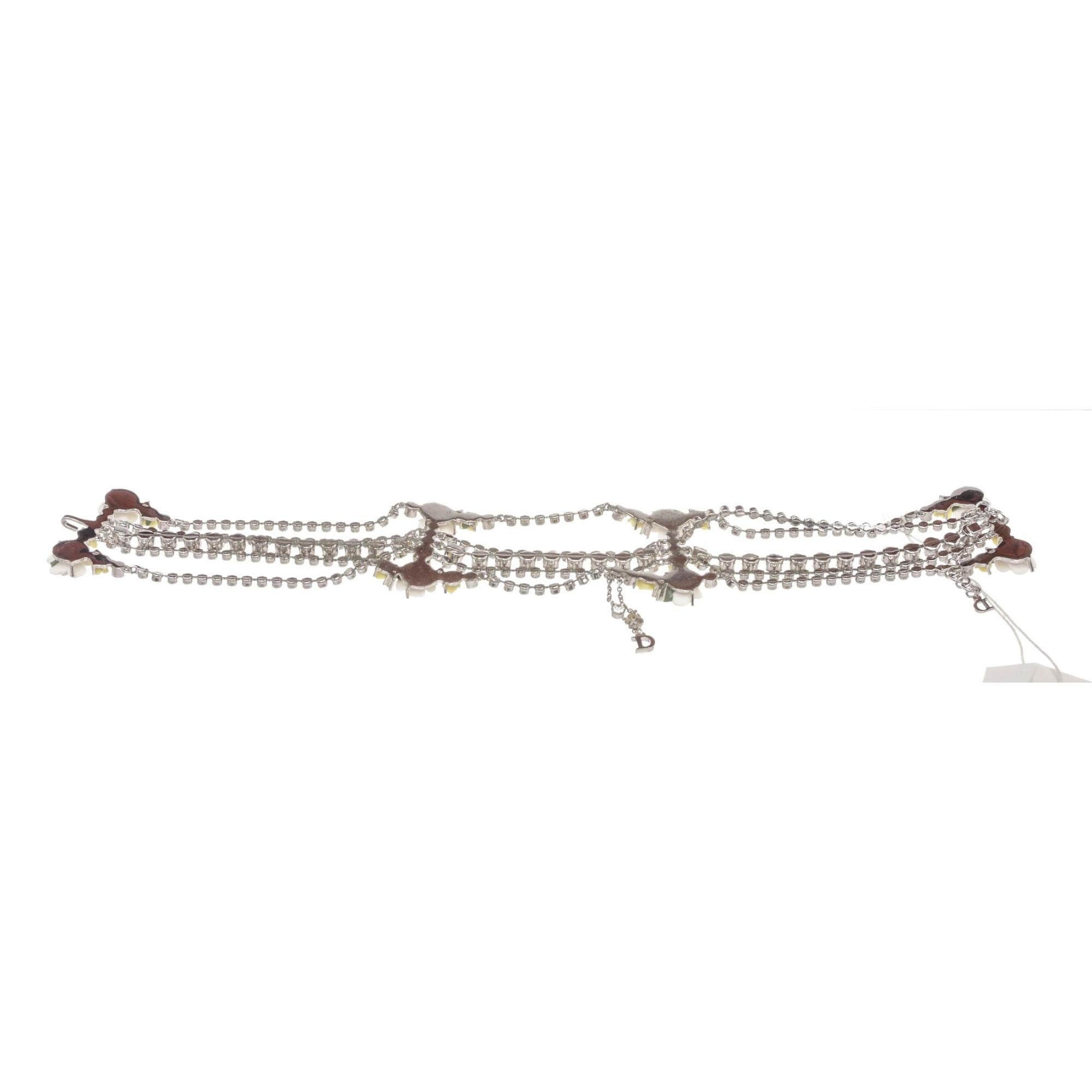 This Dior choker style necklace is from the early 2000s by Galliano. The choker is made of metal, crystal and resin. The piece features white and yellow flowers with five strands of crystals in silver with a silver CD logo charm hanging from the