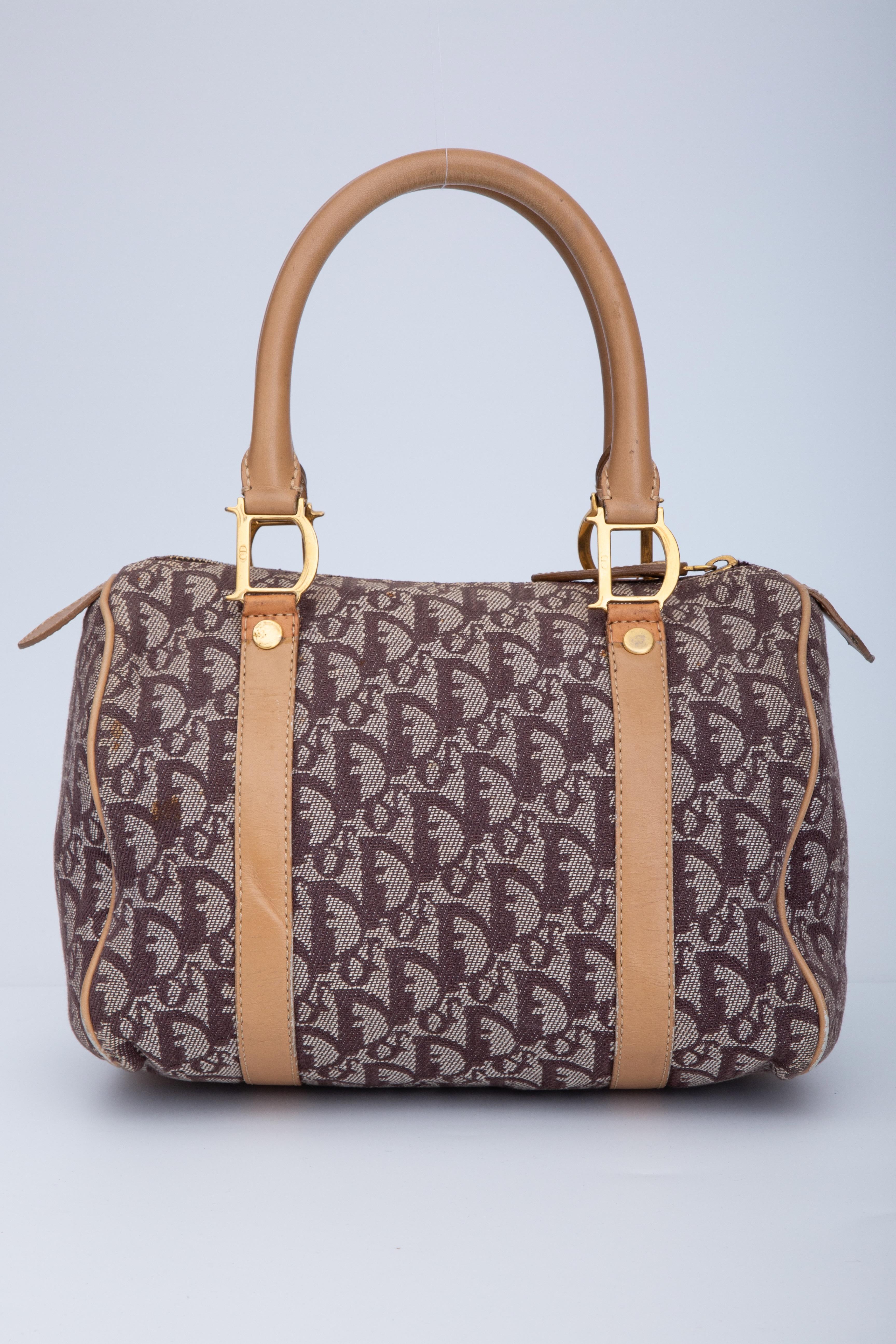 This Boston style bag from Dior measures 25-cm (9.8in), thus the name is Boston 25. The bag is made with brown and beige Trotter monogram print with leather finishes. The bag features dual rolled leather top handles, logo link attachments for the