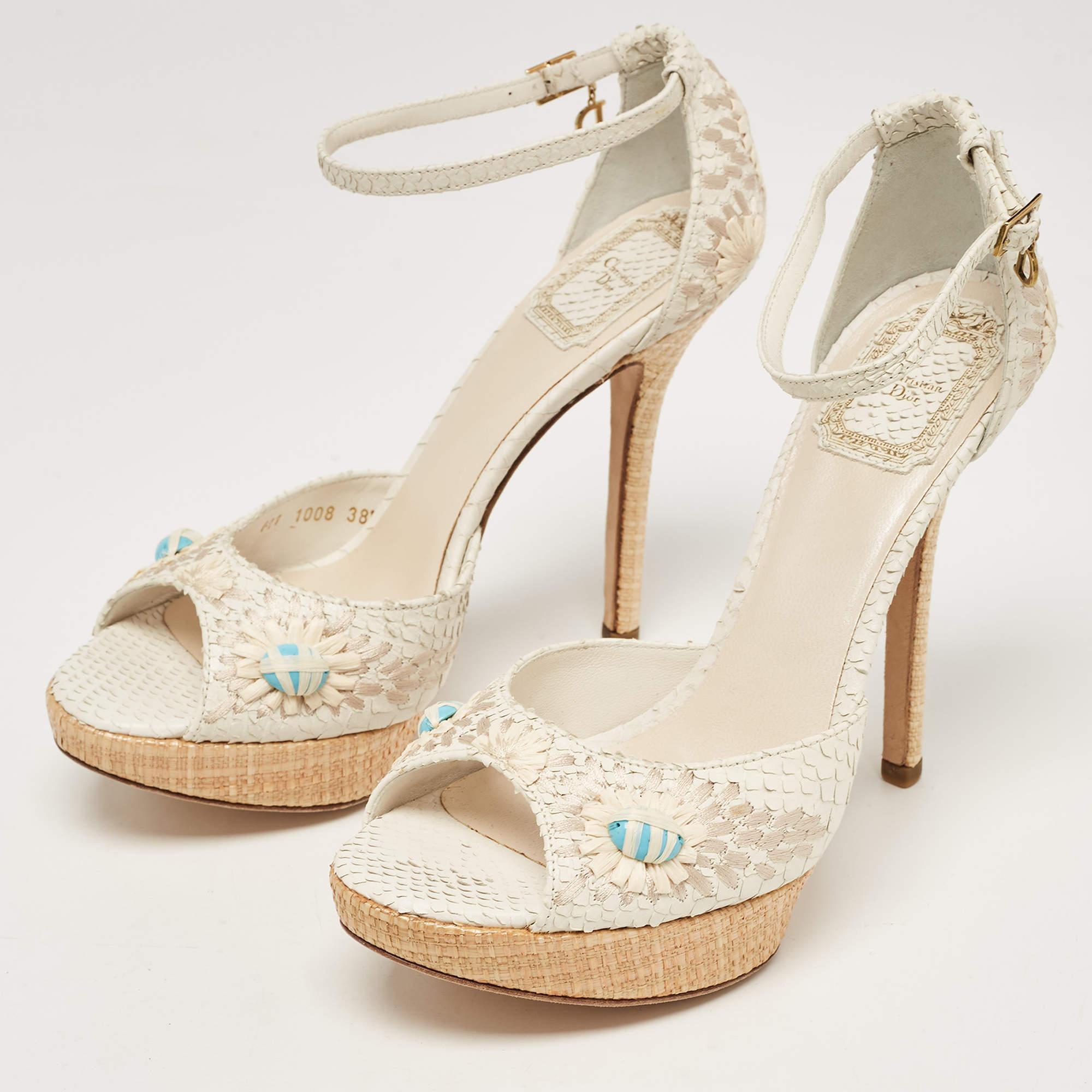 The Dior sandals feature a luxurious blend of white python leather and intricate floral embroidery. Elevated on a raffia platform, these sandals boast a stylish ankle strap for a sophisticated and fashion-forward statement.

