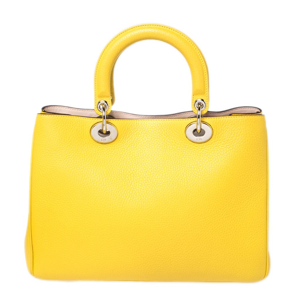 The Diorissimo shopper tote from Dior is a piece that has never gone out of style. The leather bag comes in a pleasing yellow shade with gold-tone hardware and Dior letter charms. It features double top handles, a small pouch, and protective feet at