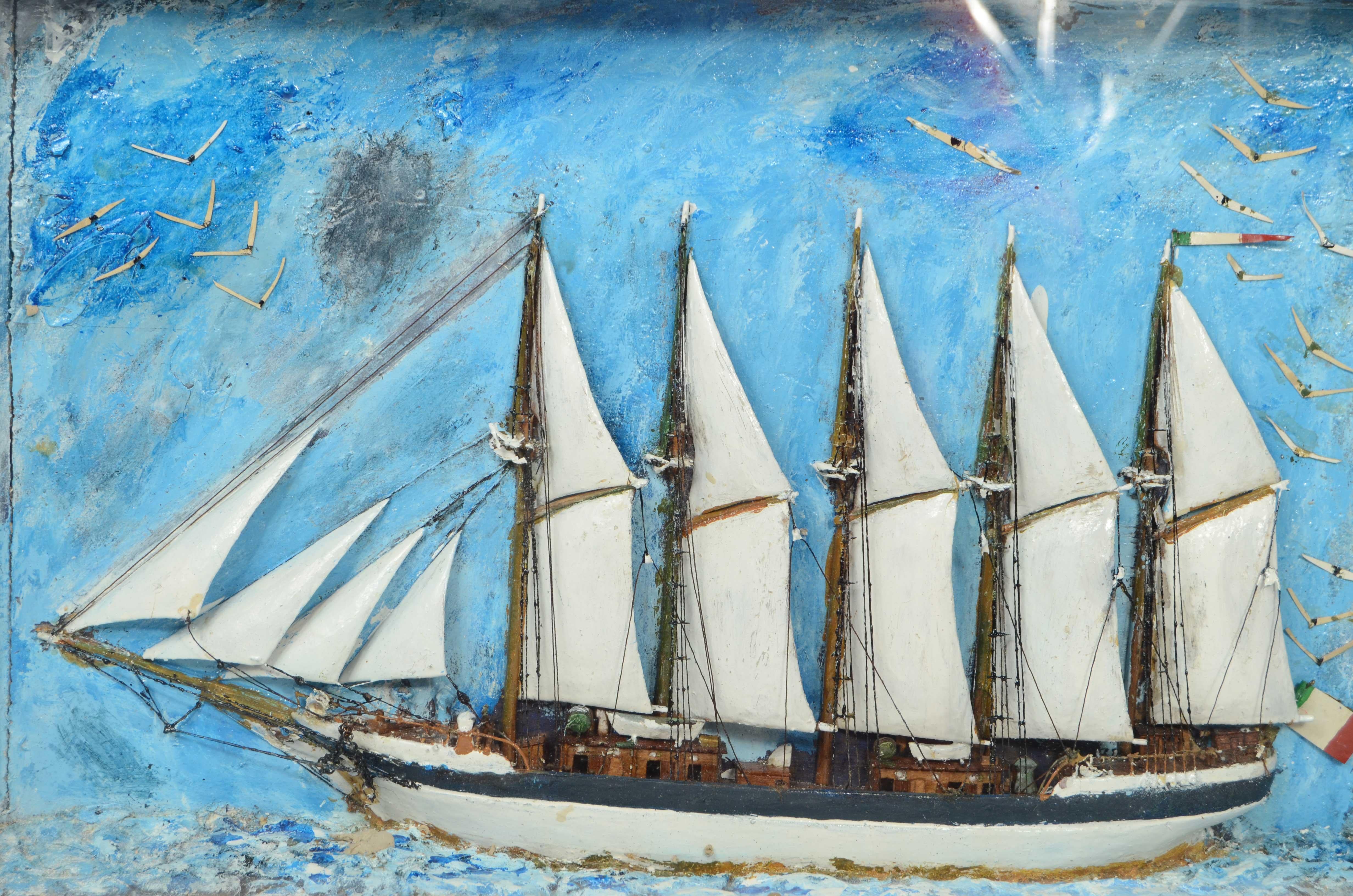 Diorama nautique logé dans un coffret en bois et en verre de forme trapézoïdale, représentant la demi-coque d'une goélette à 5 mâts avec des voiles déployées en balsa, battant pavillon italien.
En arrière-plan, la mer et le ciel bleus et de nombreux
