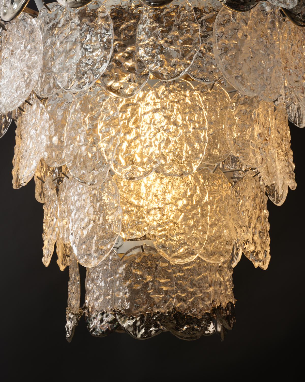 The Dip Chandelier is a remarkable addition to any ceiling plan. Its hand made Pressed Glass elements can be custom made to a variety of colors. The name derives from the process the Artist uses of dipping the glass into metal ,to leave a luster and