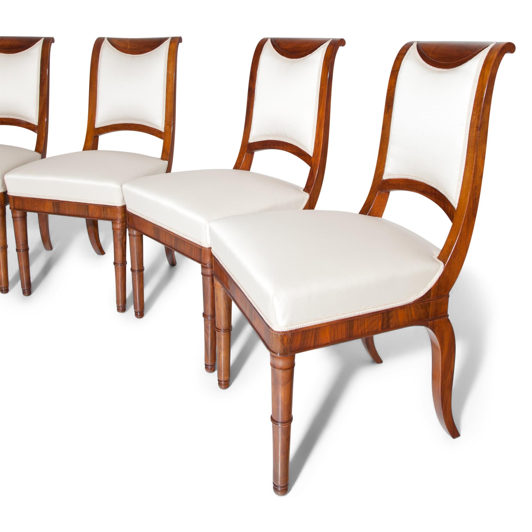 Four French Directoire walnut chairs with a cushioned S-shaped backrest and a trapezoidal seat, standing on conical feet in the front and saber legs in the rear. The chairs were professionally refurbished and reupholstered with a high quality beige
