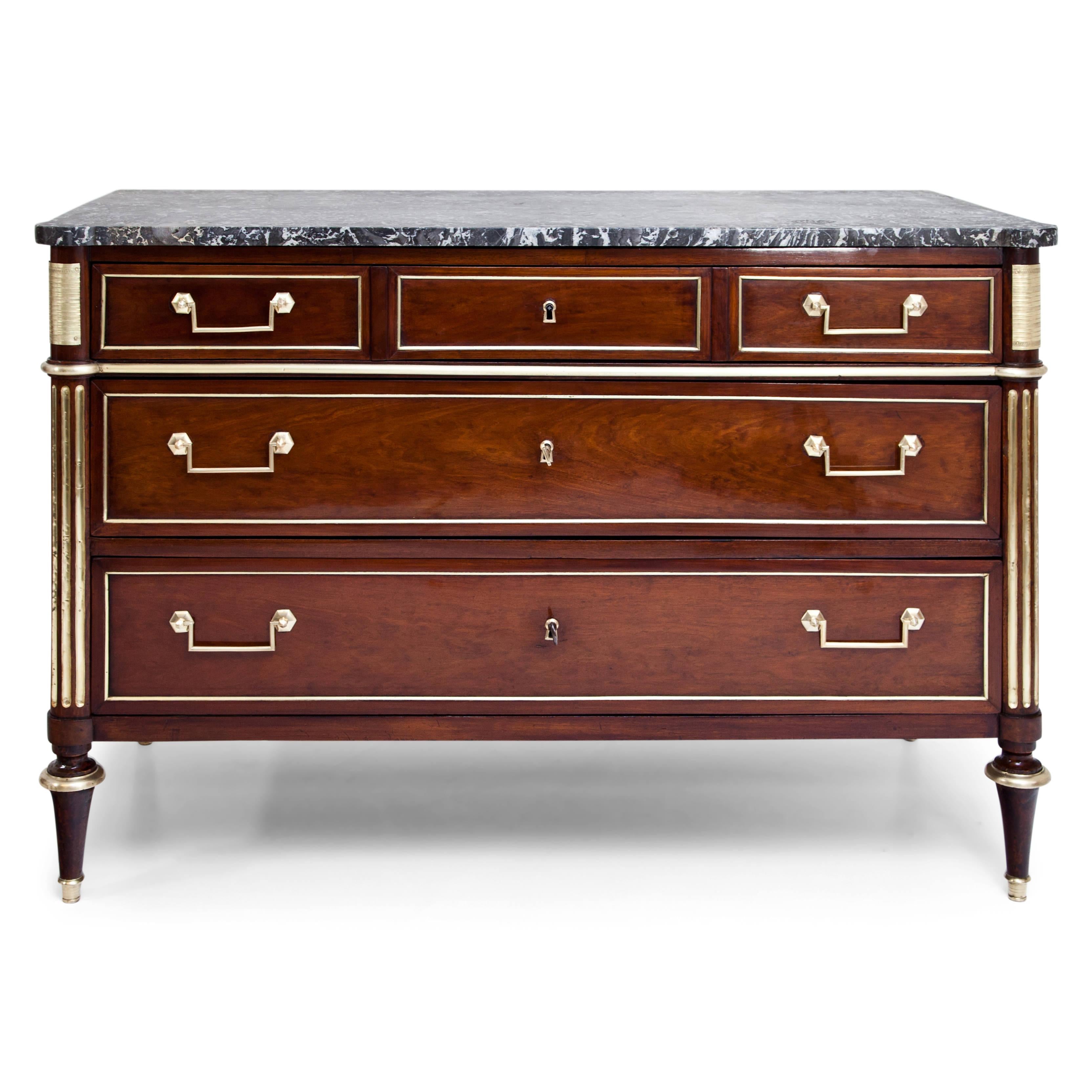 Three-drawered Directoire mahogany chest of drawers with grey-white marble top on conical legs with brass sabots, the corners in fluted three-quarter columns with brass fittings. The drawers with brass profiles, the top one visually divided into