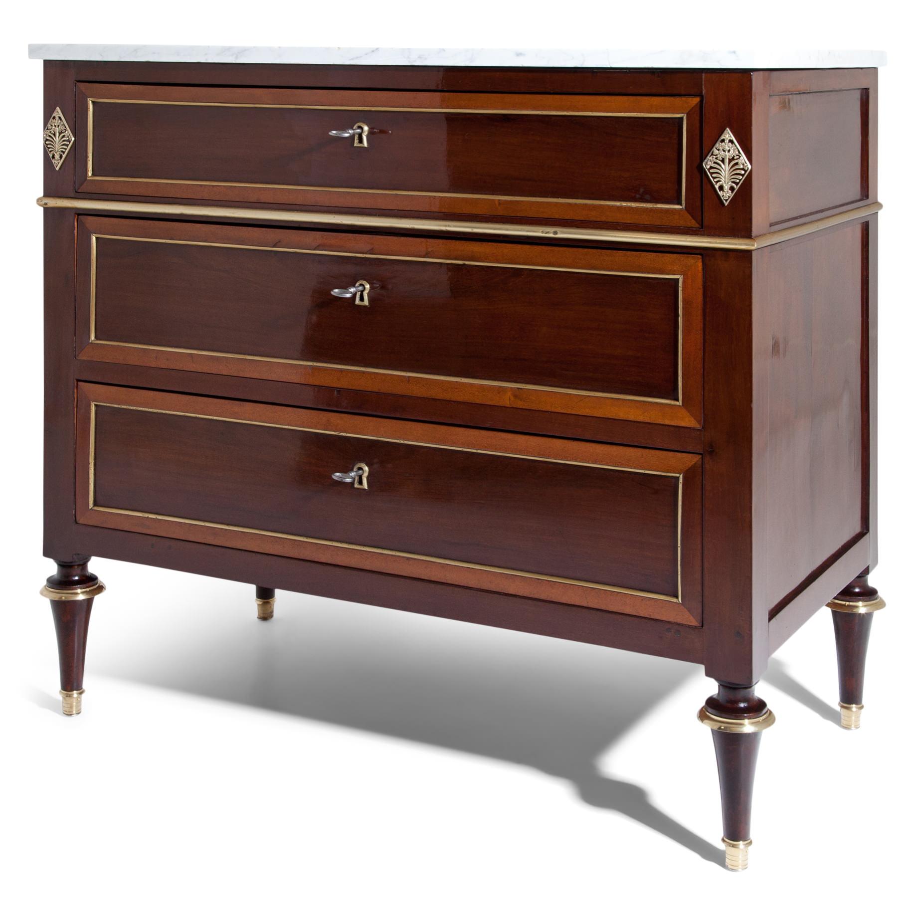Three-drawered mahogany chest of drawers on conical feet with brass details, the fillings on the drawers are also framed with brass strips. The top drawer is slightly different in size and optically set off by a brass profile and fittings. The body