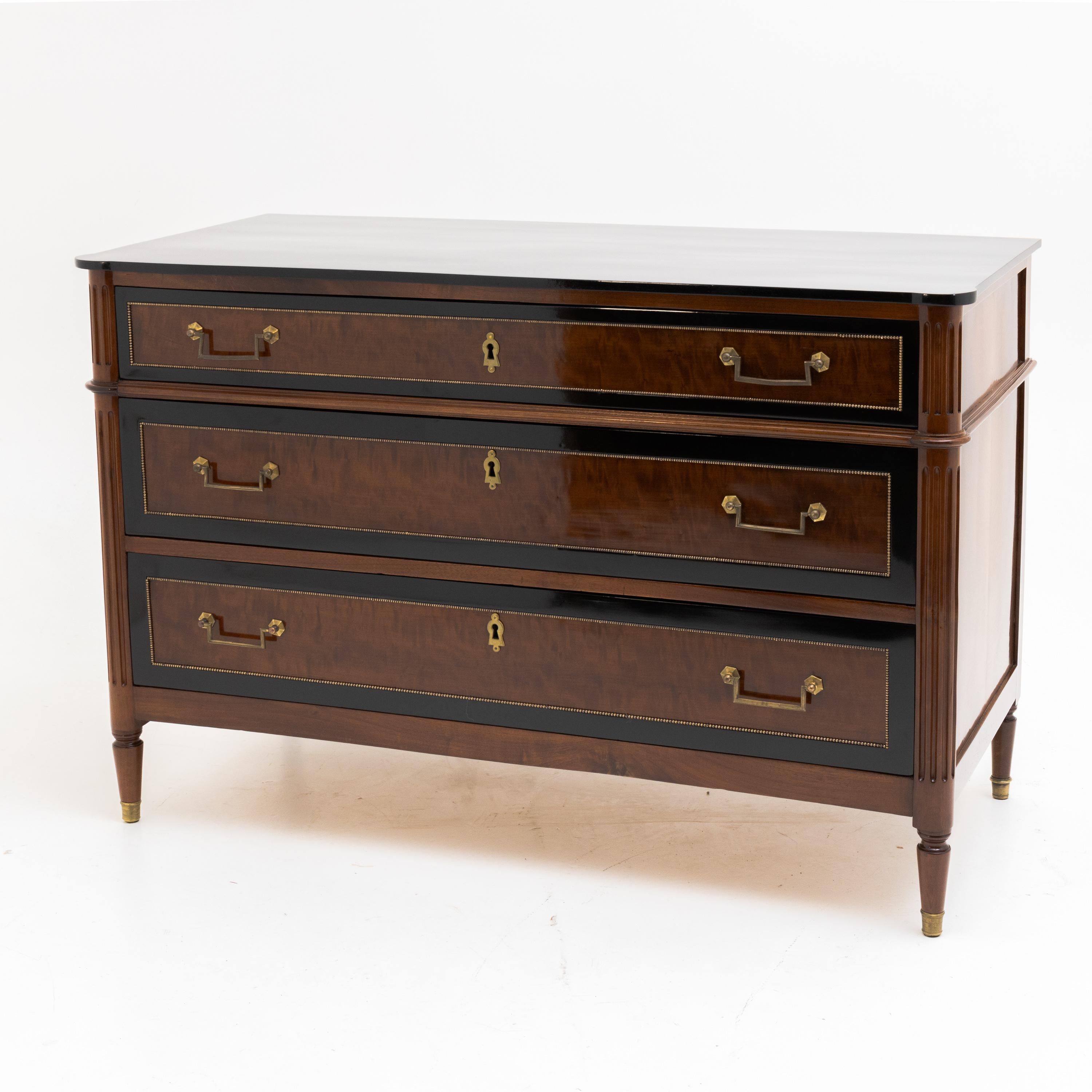 French Directoire chest of drawers on conical pointed feet with brass sabots as well as fluted, rounded corners and profiled rail in the upper third. The three drawers with darkly offset framing as well as brass bead moldings are veneered in
