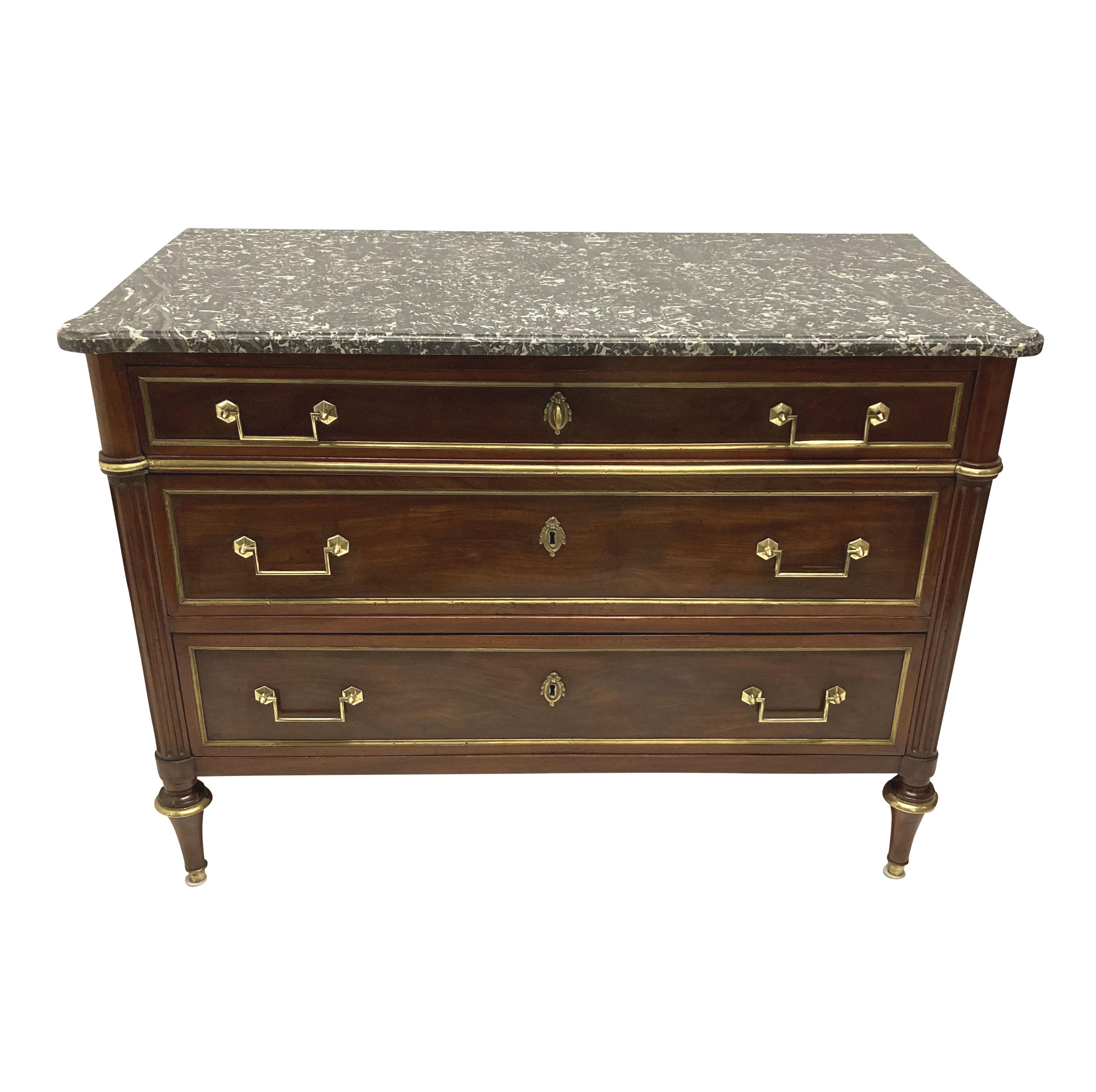 Commodo Direttorio francese a tre cassetti in mogano, con montature e intarsi in ottone e piano in marmo grigio chiaro variegato sagomato.