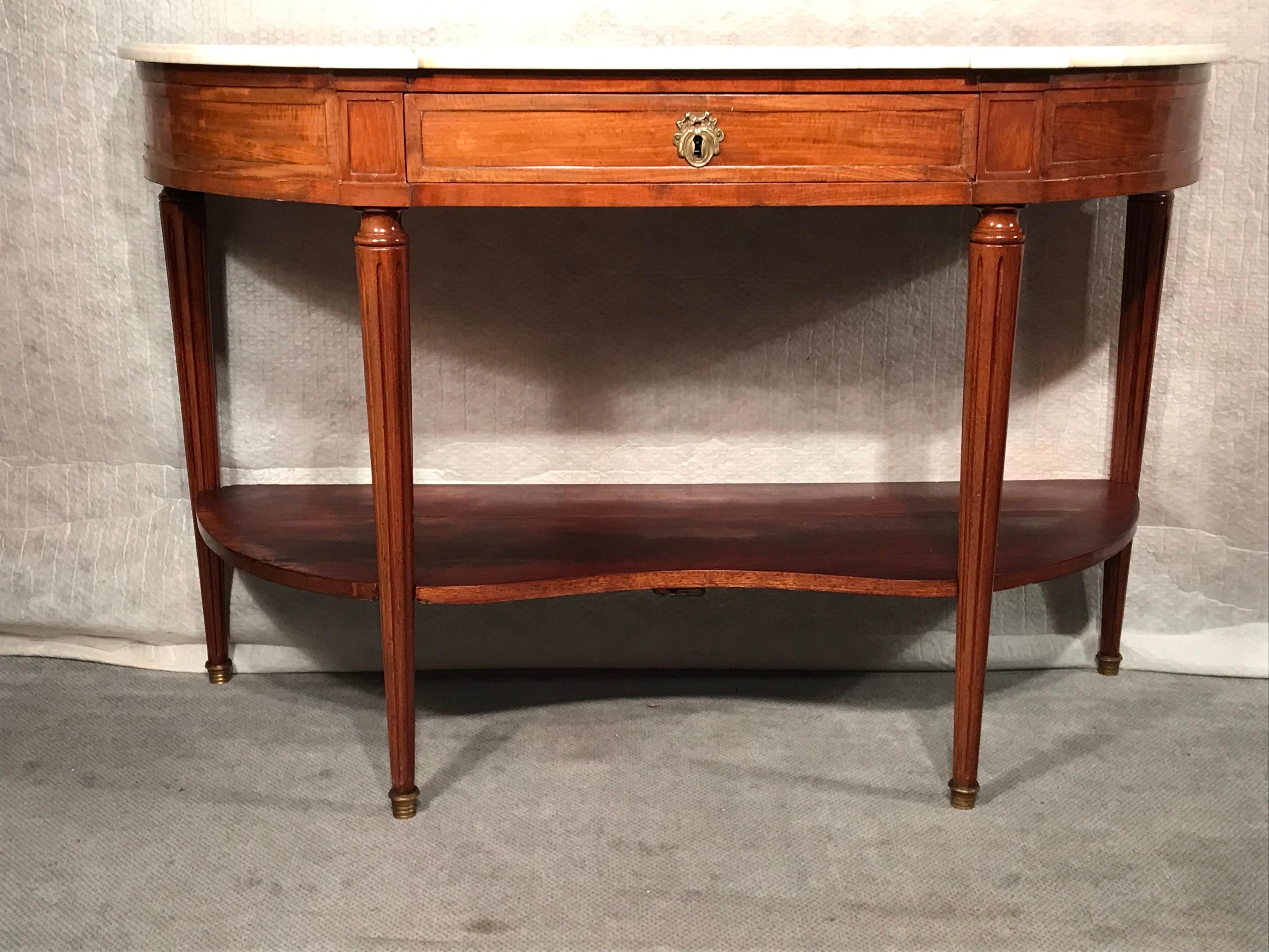This elegant French Console table dates back to the first quarter of the 19th century. The Directoire console table has a pretty mahogany veneer. The Demi lune table stands on fluted legs. It has a white marble top and one mahogany etagere in the