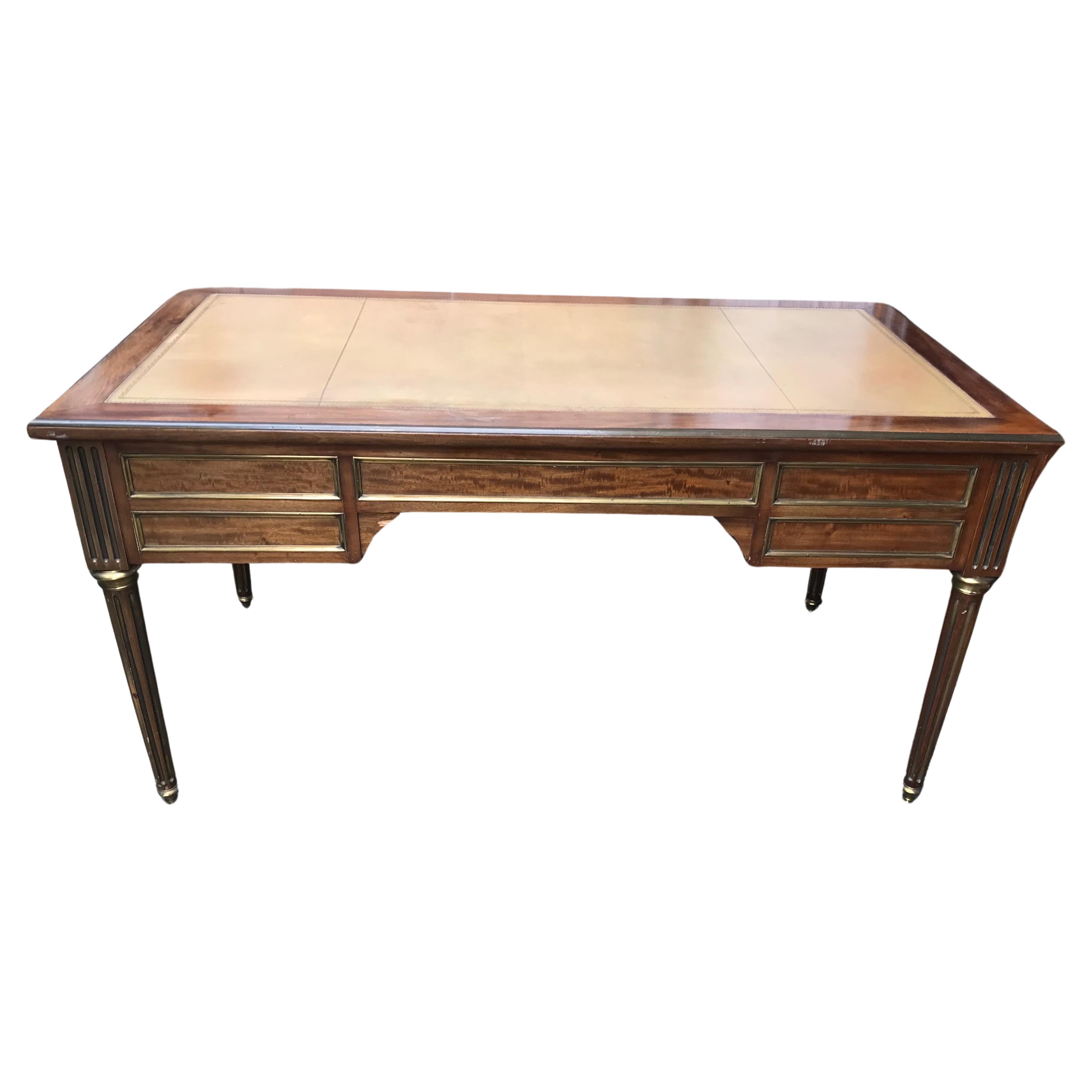 This elegant Directoire style desk dates back to the second half of the 19th century. The desk has a pretty mahogany veneer and is additionally embellished with brass fillets. The top is covered with light brown leather and has two additional