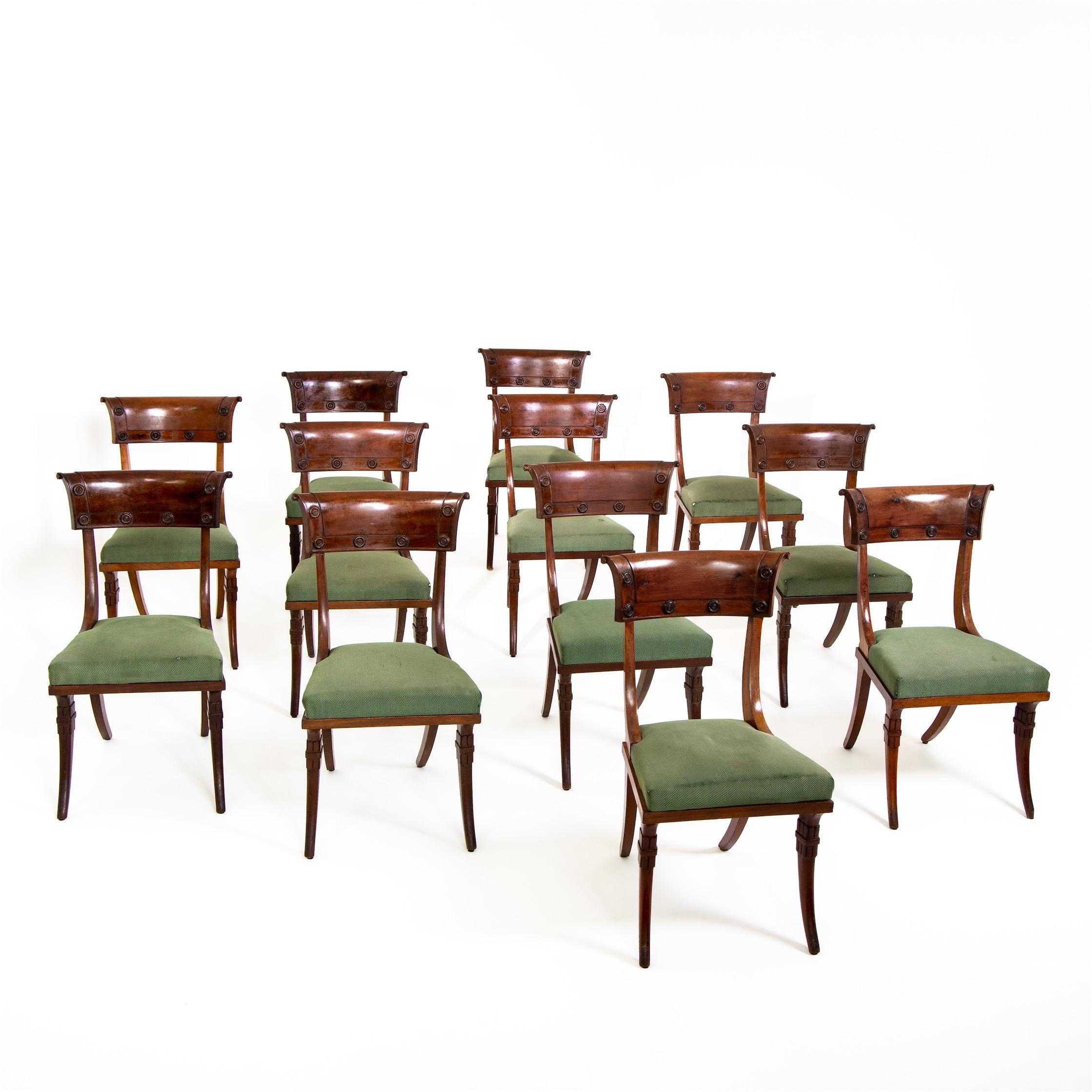 Set of 12 Directoire chairs in unrestored condition. The design echoes the Greek Klismos chair with strongly flared conical pointed legs on both sides and the reduced backrest with rounded board with disc ornaments.