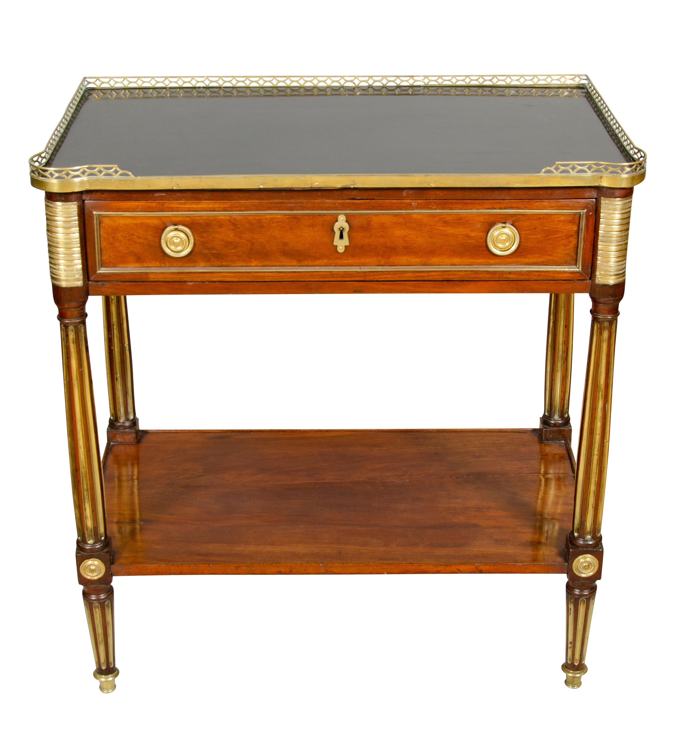 With rectangular top with 3/4 brass gallery and dark grey stone top over a drawer with two circular gilt bronze ring handles, raised on circular brass inset fluted legs joined by a lower shelf, raised on conforming fluted legs.