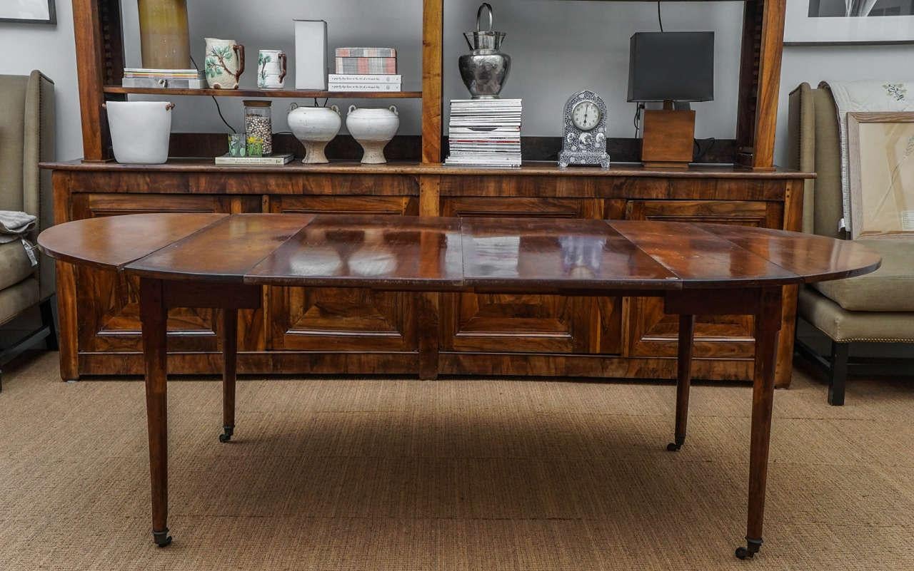 Lovely directoire mahogany drop-leaf extending dining table. Oval table top rests on four ring turned tapering legs that terminate in brass caps and castors. Each drop-leaf measures: 24