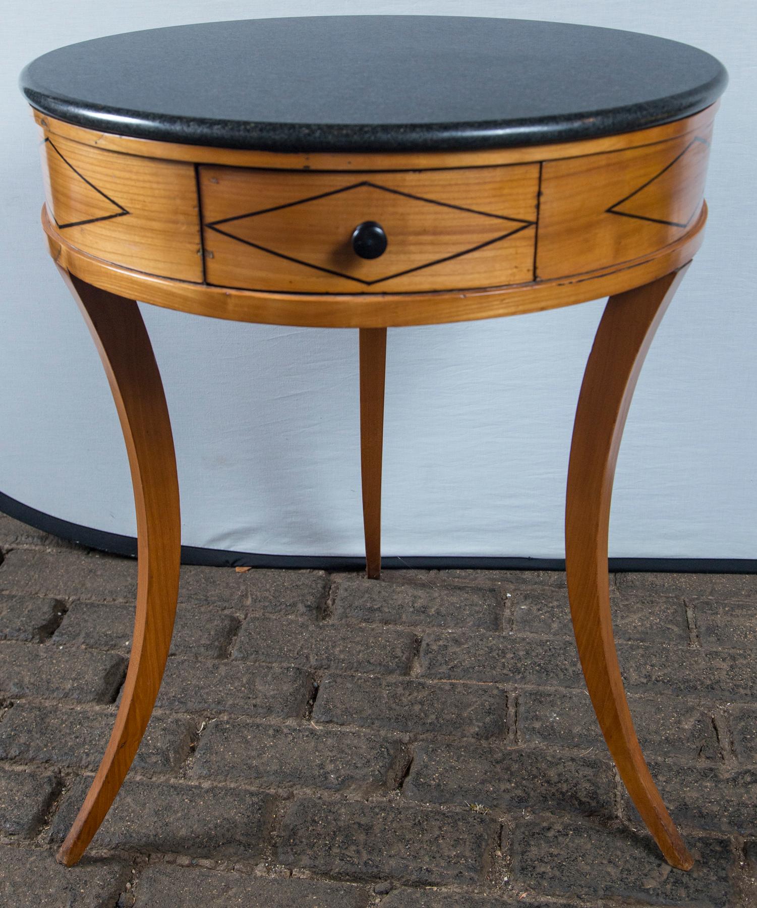 Black marble-top round wood Directoire table with delicate splayed legs, center drawer, ebony wood marquetry.