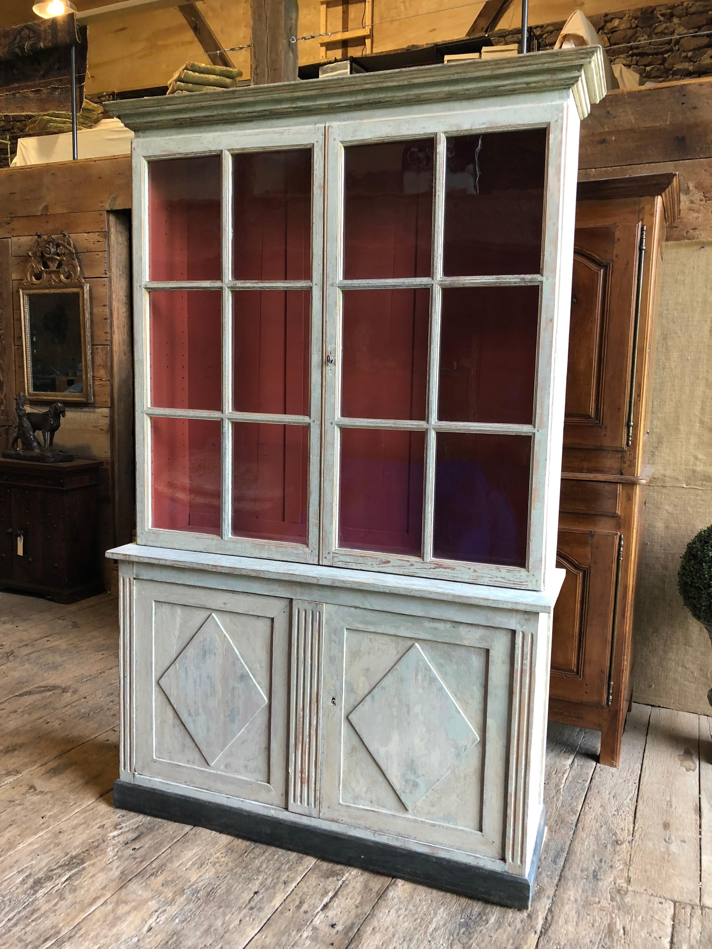A wonderful and rare French Directoire Period bookcase cabinet in 2-parts, circa 1800, hand-scraped to its original grey painted finish, and retaining its original wavy glass panes. 
The lower cabinet has a single shelf and the doors are decorated