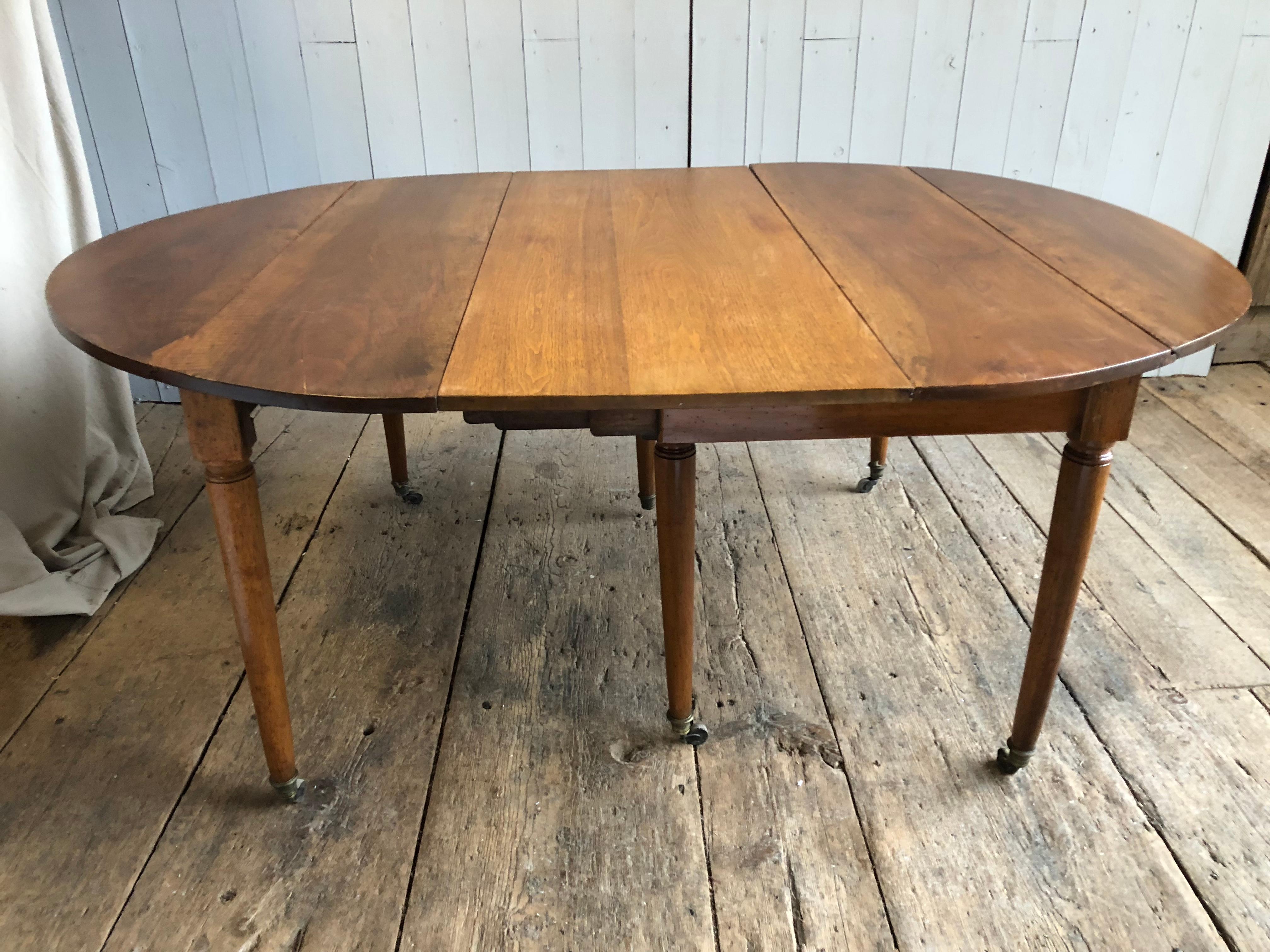 A French Directoire Period, circa 1800, drop-leaf expandable dining table in light walnut, with additional leaf (later). The table has 6 simple turned and tapered legs on casters two of which are a pair of center support legs for when expanded.