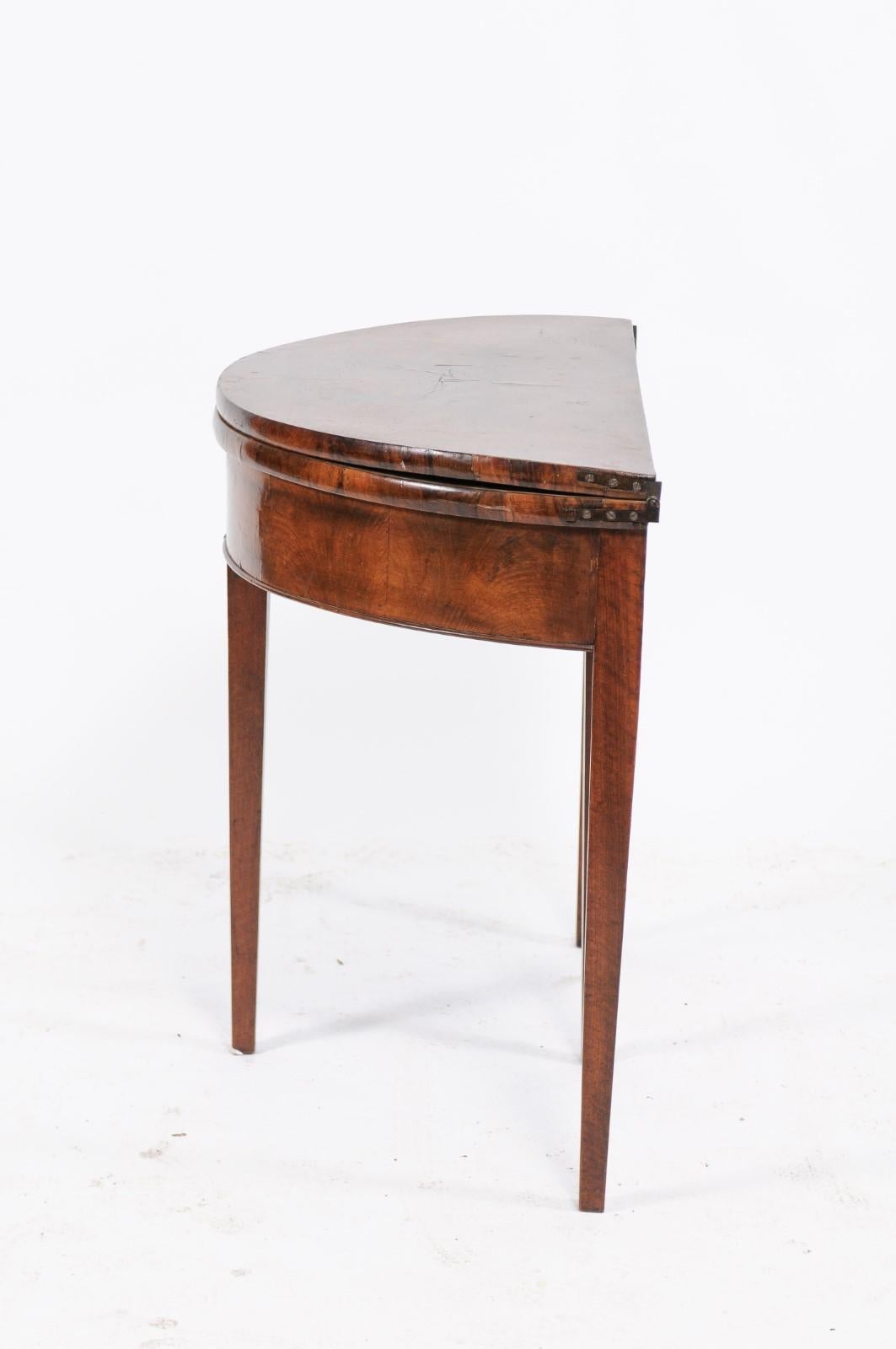A French Directoire style bookmark walnut veneered demilune console table from the third quarter of the 19th century, with folding top, leather inset and tapered legs. We loved the simple lines and rich patina of this walnut folding demilune console