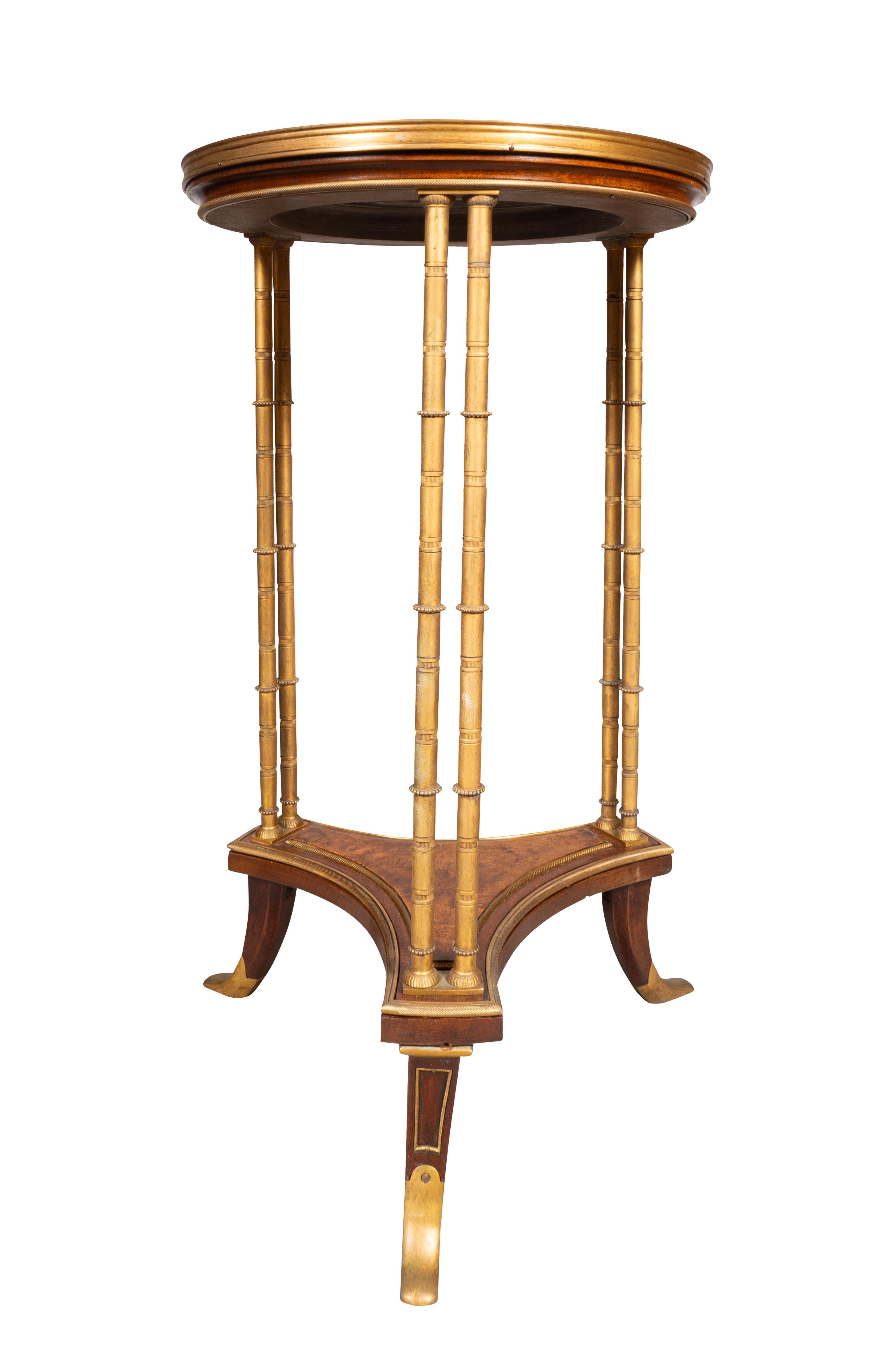 Circular inset black granite top with metal banded edge and three faux bamboo cluster column supports joining a lower tripartite stretcher. Ending on bronze capped saber legs.
