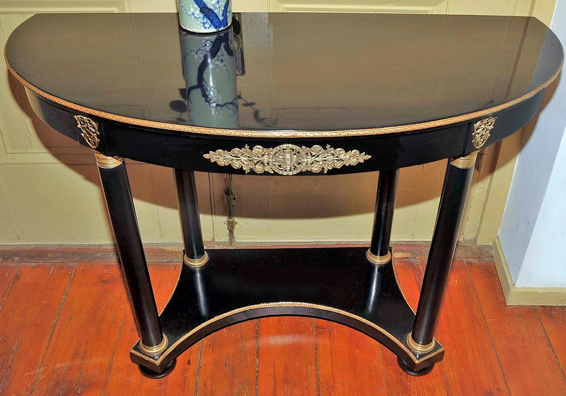 Vintage midcentury Classic table with gilt bronze banded ebonized top. The demilune apron is fitted with bronze mounts. There are four column legs with bronze chased capitals and bases. The second shelf is concave and banded in gilt bronze on bun