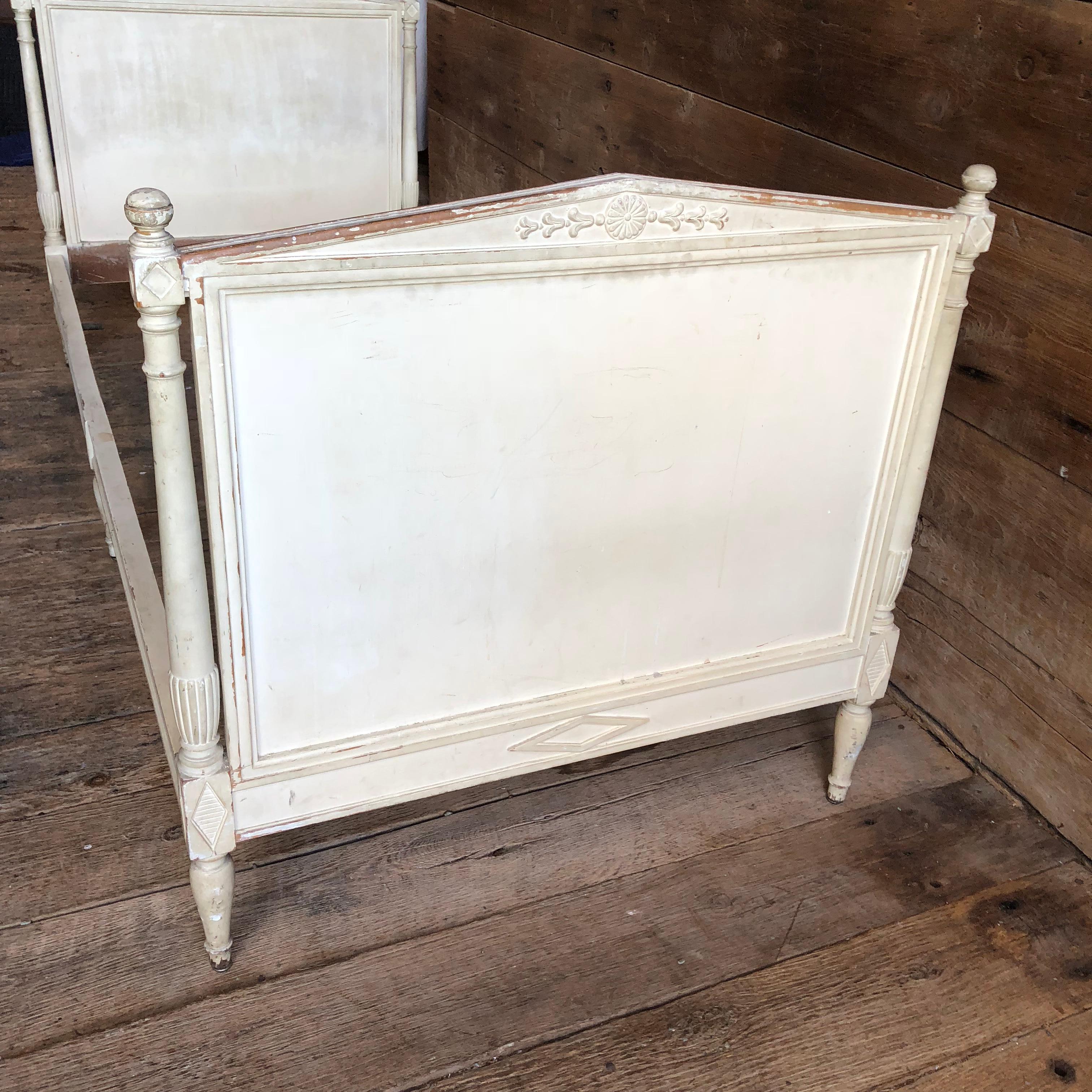 A French 19th century Directoire style painted daybed in a nice petite size, old cream painted finish with patina, the diamond crested headband footboards with turned ball finials and central carved rosettes, turned columns, on urn form feet, the