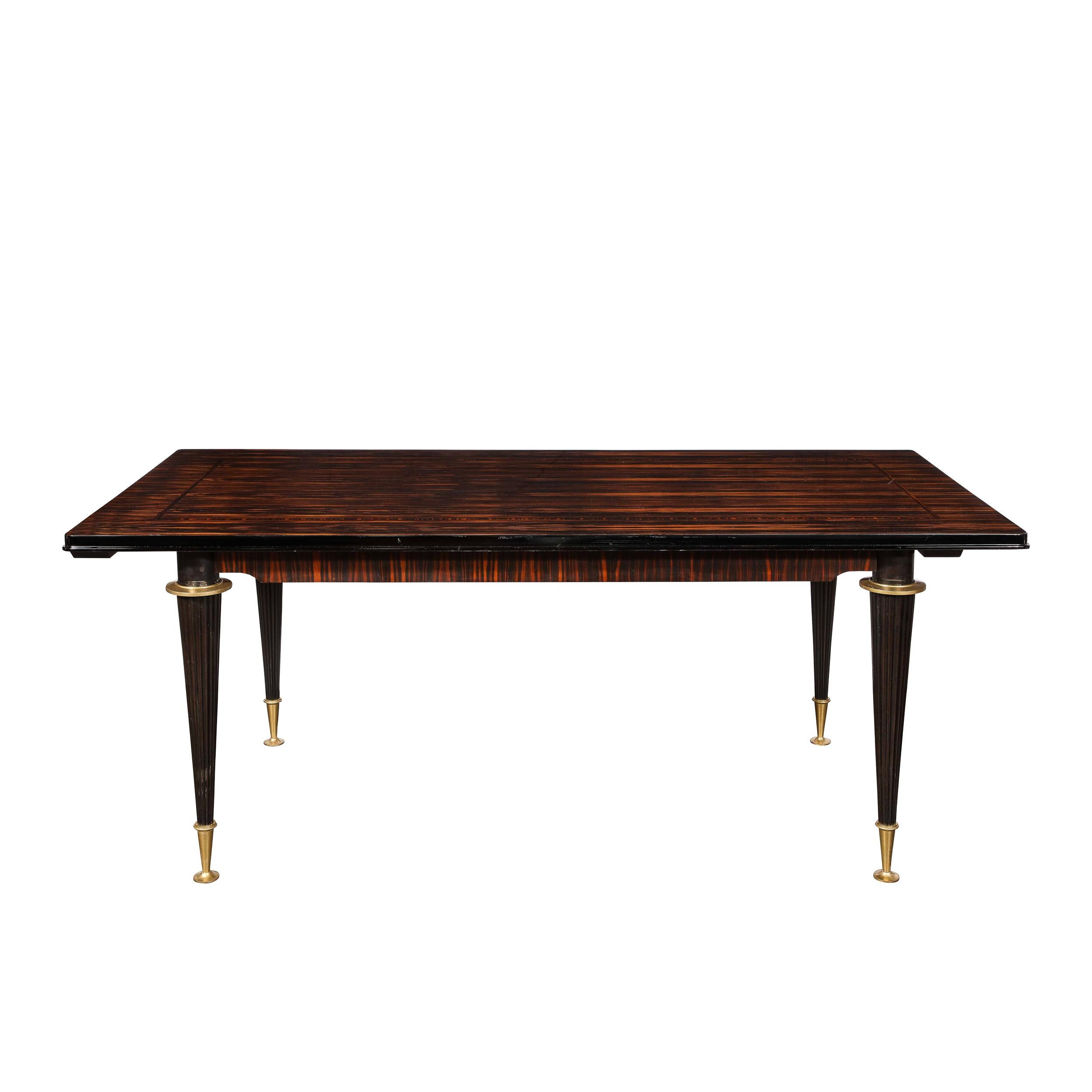This stunning Art Deco dining table was realized in France circa 1940. Sitting on four conical ebonized legs with brass capped sabots and brass circular embellishments at the apex of each leg, this directoire style table features a dramatic
