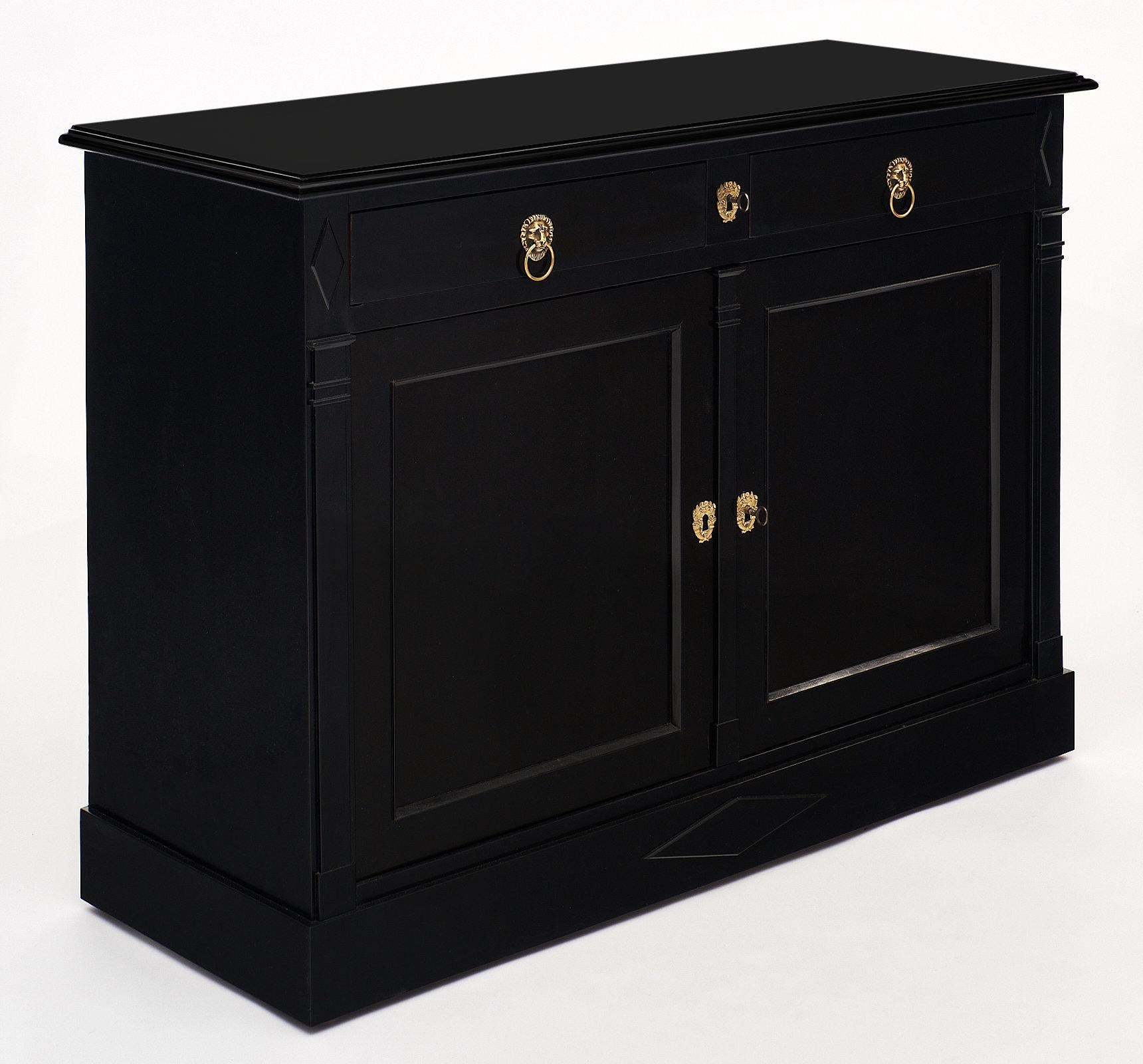 Ebonized Directoire style buffet with two doors and two drawers, finished with a lustrous French polish. The piece boasts two brass lion head pulls and three unique stylized brass escutcheons, along with two working keys. The top corners of the