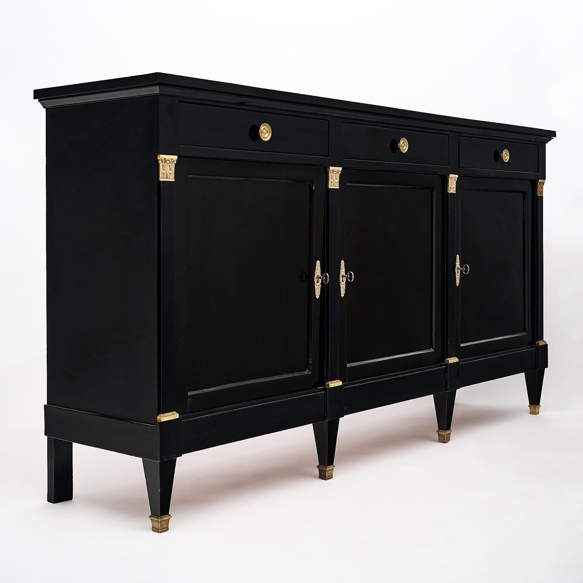 Buffet, French, in the Directoire style made of mahogany that has been ebonized and finished in lustrous museum quality French polish. Three doors open to adjustable shelving, while three dovetailed drawers sit atop. The square tapered legs and