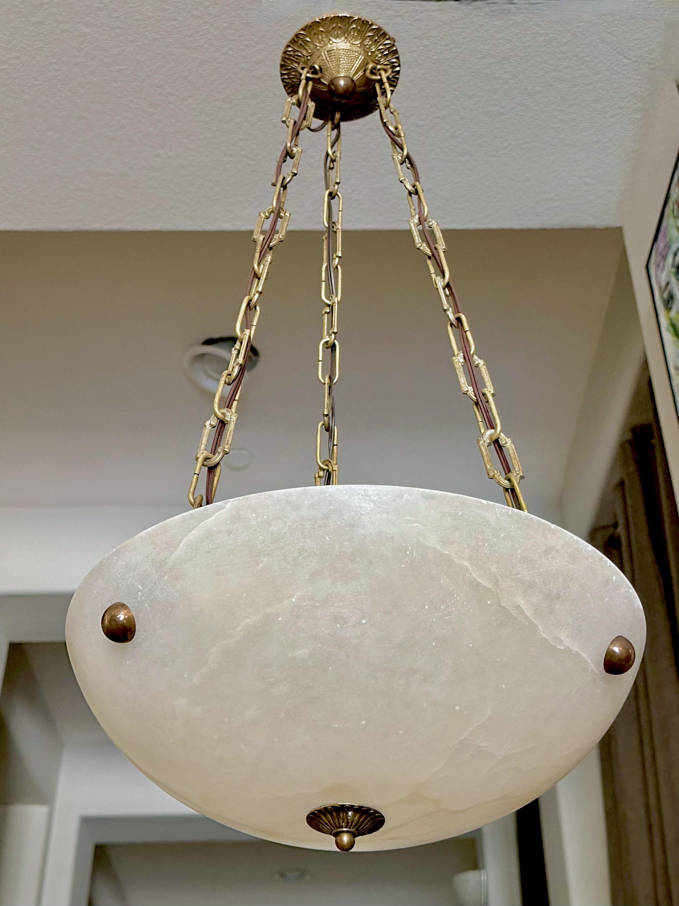 Suspension française en albâtre avec des ferrures en laiton vieilli (antiqued) dans le style Directoire. L'éclairage intérieur utilise 3 ampoules de taille candélabre (LED recommandées). Câblage récemment effectué. 
Le bol en albâtre date des années