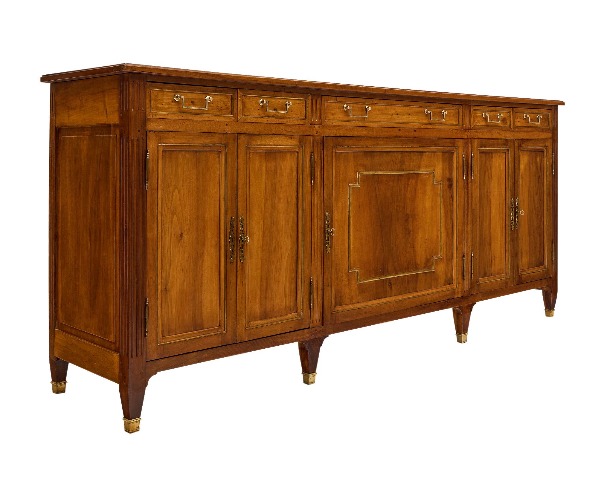 Buffet from France in the Directoire style. This warm walnut piece has five dovetailed drawers above three sets of doors that open to interior shelving. The case piece features brass hardware and trim throughout. It is supported by tapered legs, six