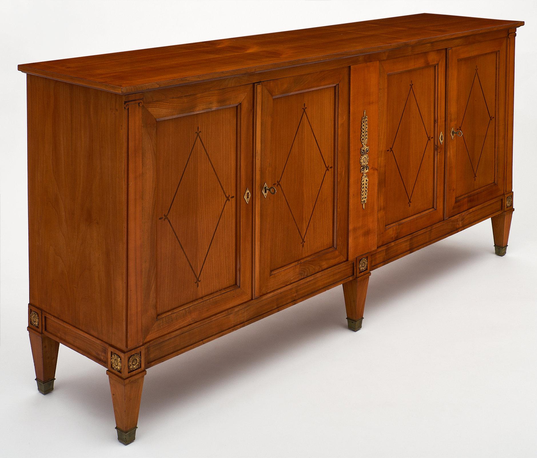 French Directoire style cherrywood buffet with ebony inlay on the doors. We love the beautiful bronze hardware and Classic details of this elegant piece. The doors have working locks and keys and open to reveal interior shelving. This piece has been