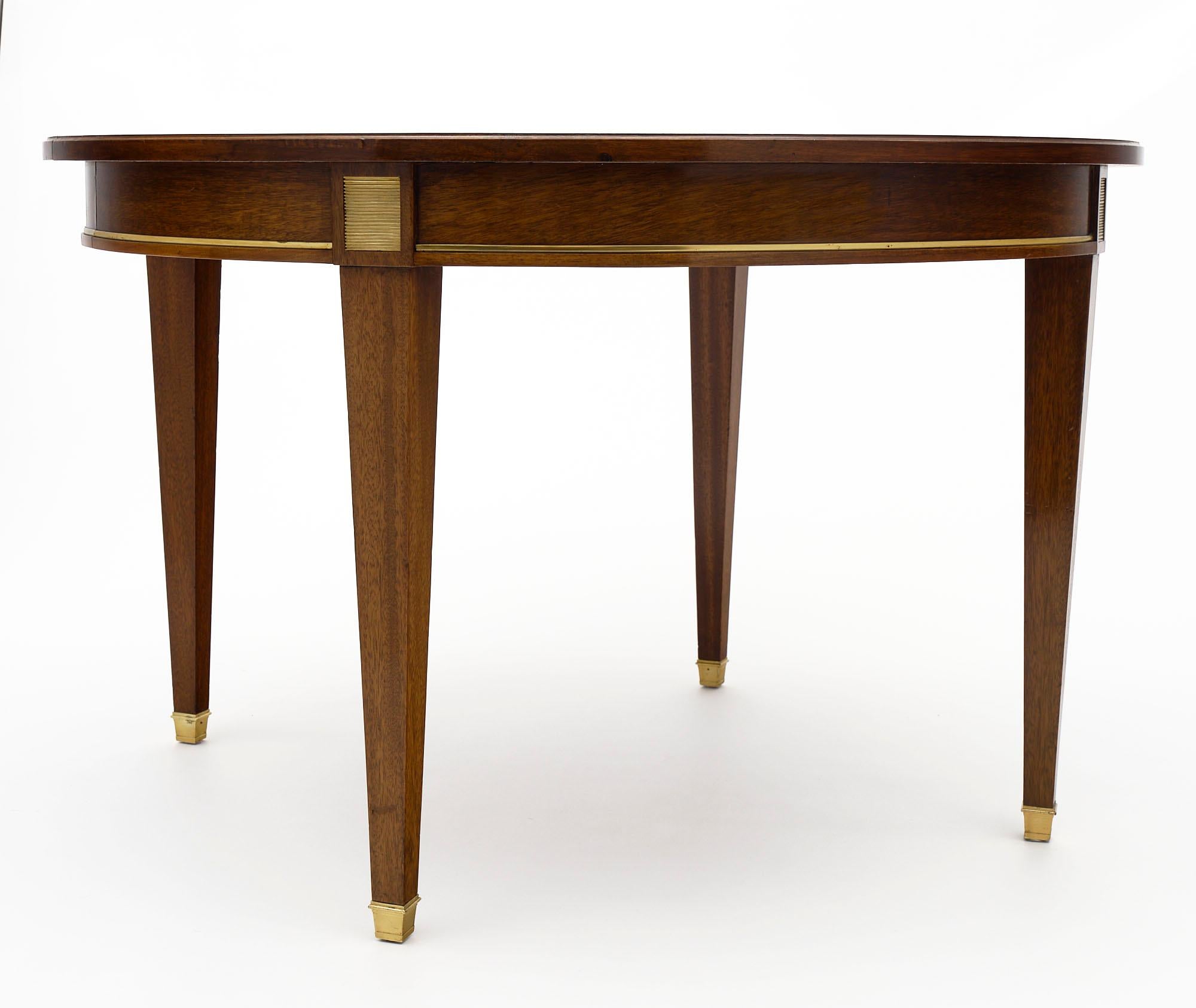 Dining table in the French Directoire style made of walnut featuring brass trim around the apron and above the tapered legs. The table could open for leaves; though we do not have the leaves available at this time. The feet are all capped with brass.
