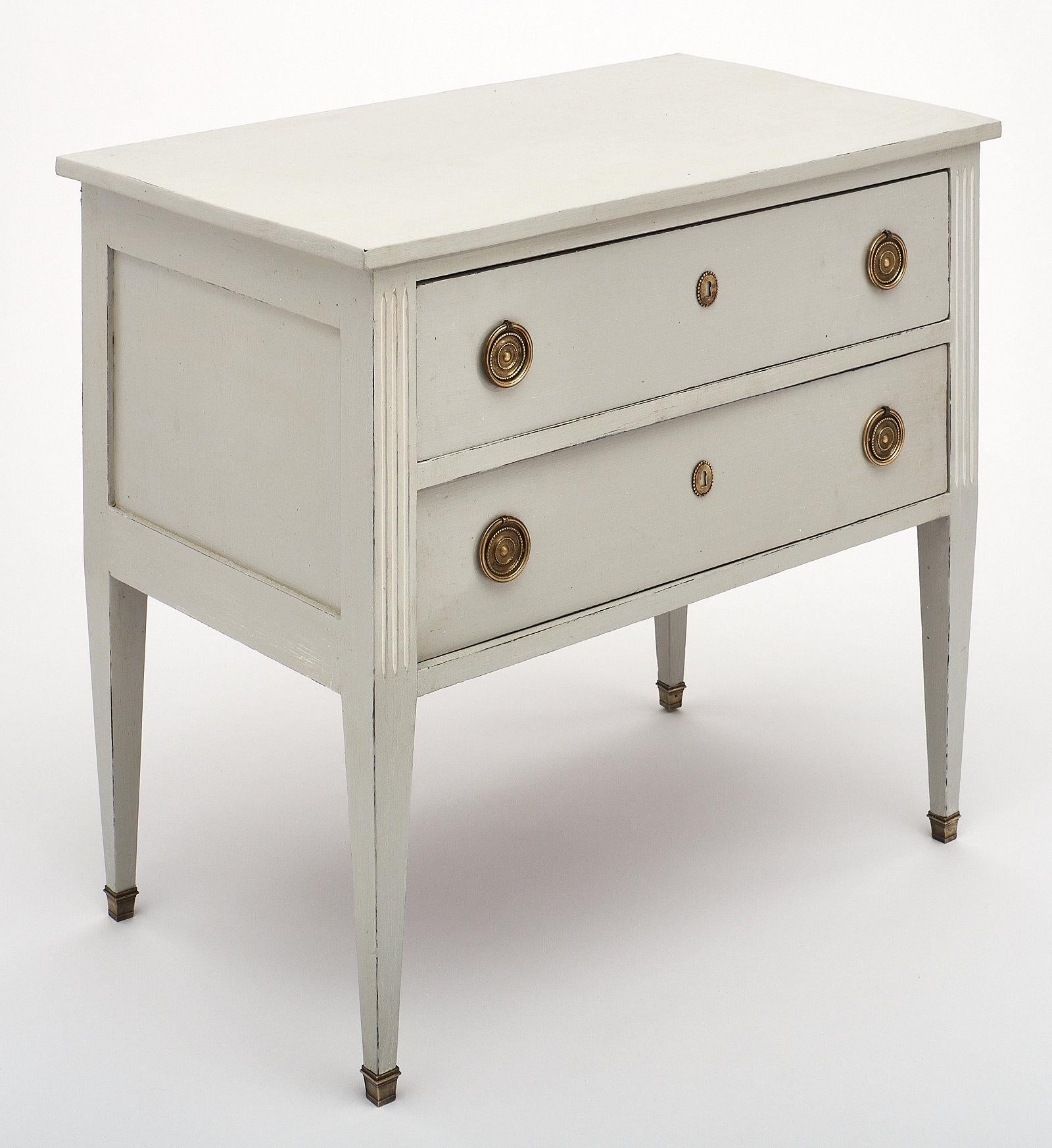 A French Directoire style painted chest of drawers with two large dovetailed drawers, tapered legs with bronze feet, and original bronze hardware. This piece is made of cherry wood. We love the dove gray color with white fluted details.