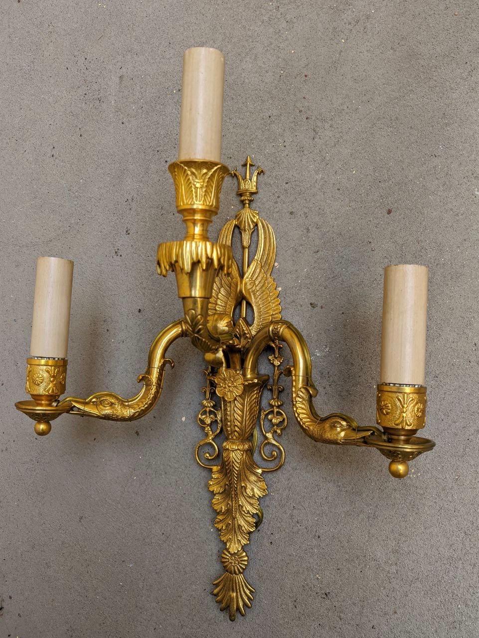 This French Directoire style sconce features top-quality chiselled bronze, with many vivid details. On the top of this sconce, there is a trident sided by two swan's wings. The body features a vegetal decoration with leaves and geometric