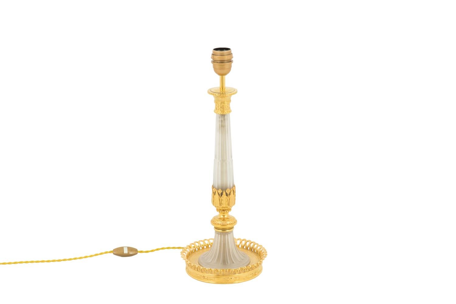 Directoire style lamp in large candleholder shape in glass and gilt bronze. Fluted baluster shape shaft in polished transparent glass topped by a capital in braided basket shape. It is finished by gilt bronze motifs of leaves, small flowers, a beads