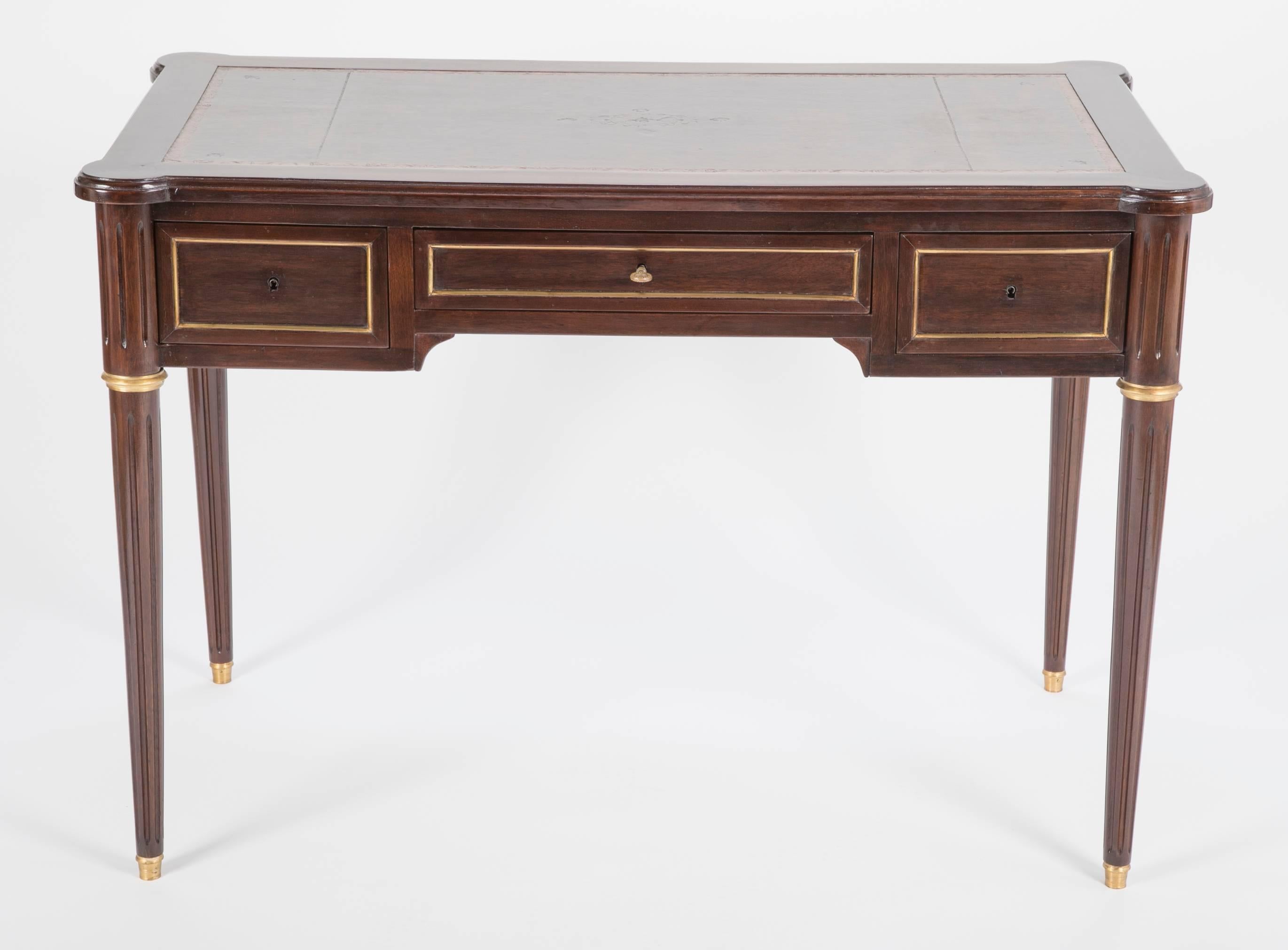 A Directoire style mahogany desk with inset leather top having three drawers and brass trim.