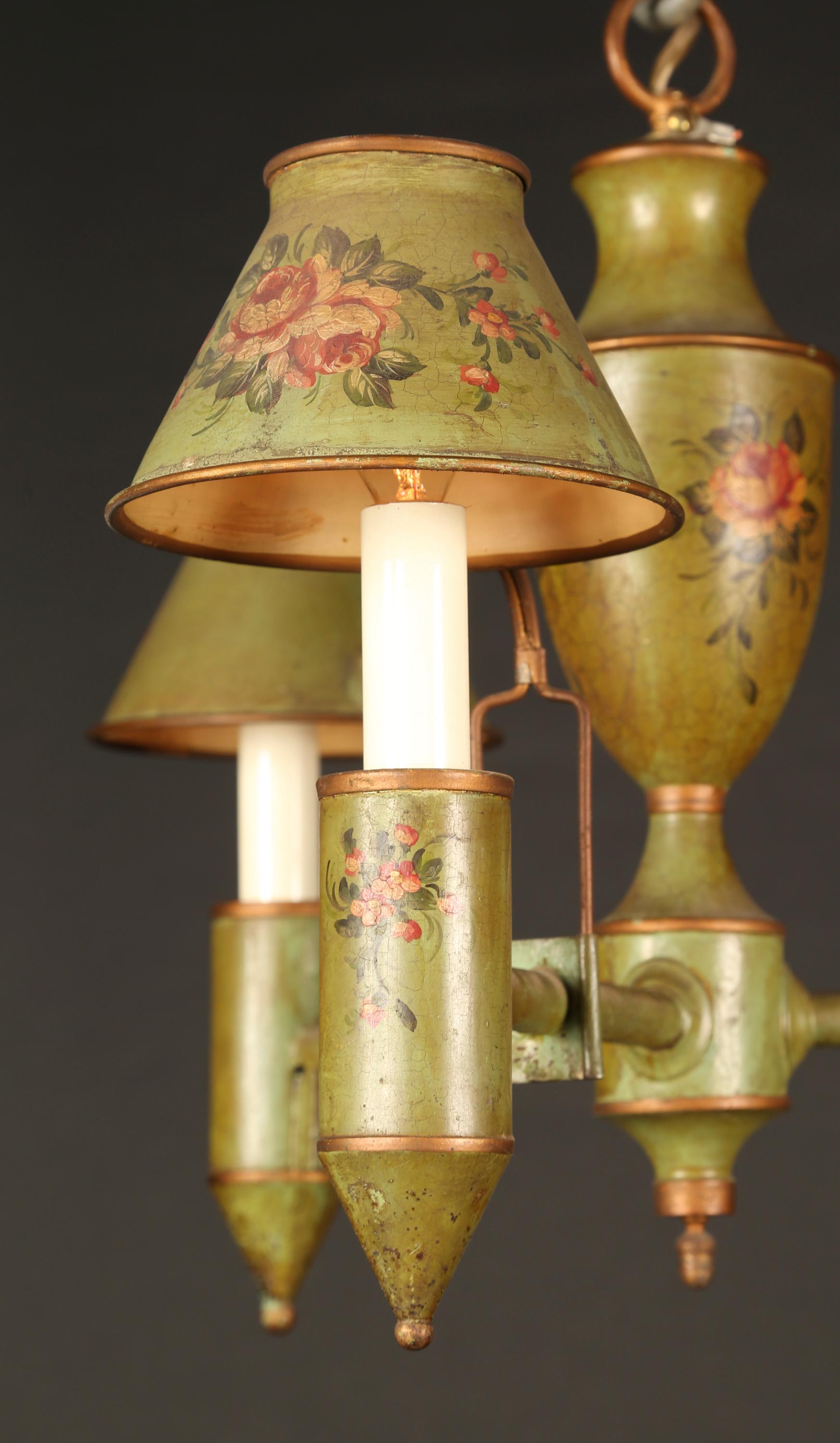 This Italian Directoire style green tole chandelier features beautiful hand painted elements and dates back to the mid 20th century. Note the painted details on the center, the candle cups, and the attached and supported tole shades. The piece has a
