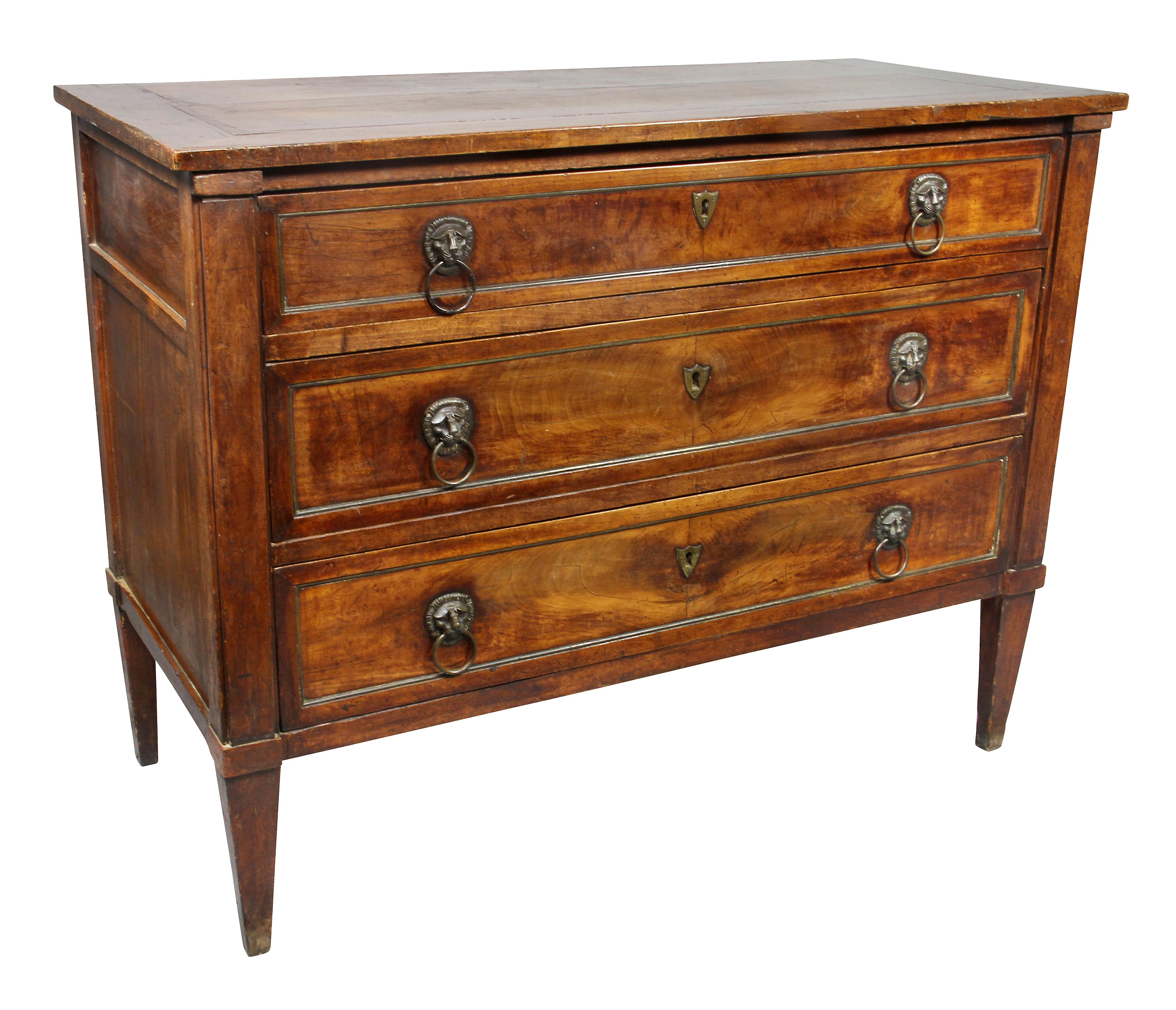 With a rectangular top over three graduated drawers with brass moldings, raised on square tapered legs. Lions head handles and shield form escutcheons.