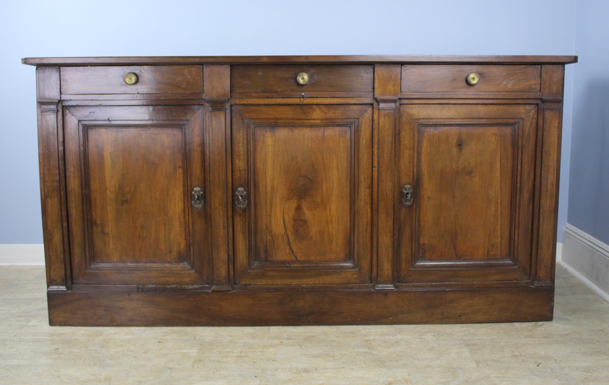 A large and imposing dark walnut enfilade, quite early. Doors have great articulated inset panels and close snugly, each with their own key. Single non-adjustable shelf in each cabinet. There is a beautiful retractable serving shelf under the center