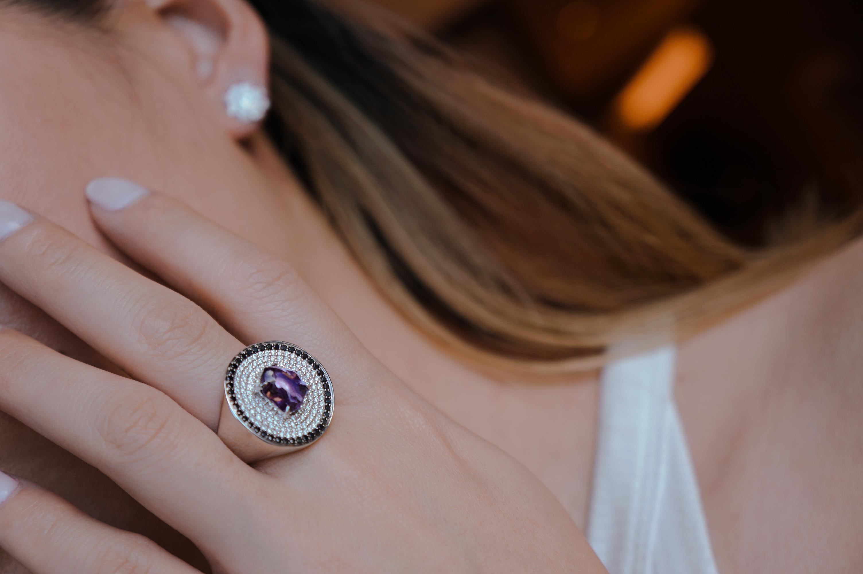 A pure circle, with concentric rings of black and white pave diamonds, creates a contrasting setting for a striking, organically shaped sapphire in Ri Noor's Disc Cocktail Ring with Purple Sapphire and Black and White Pave Diamonds. The unique