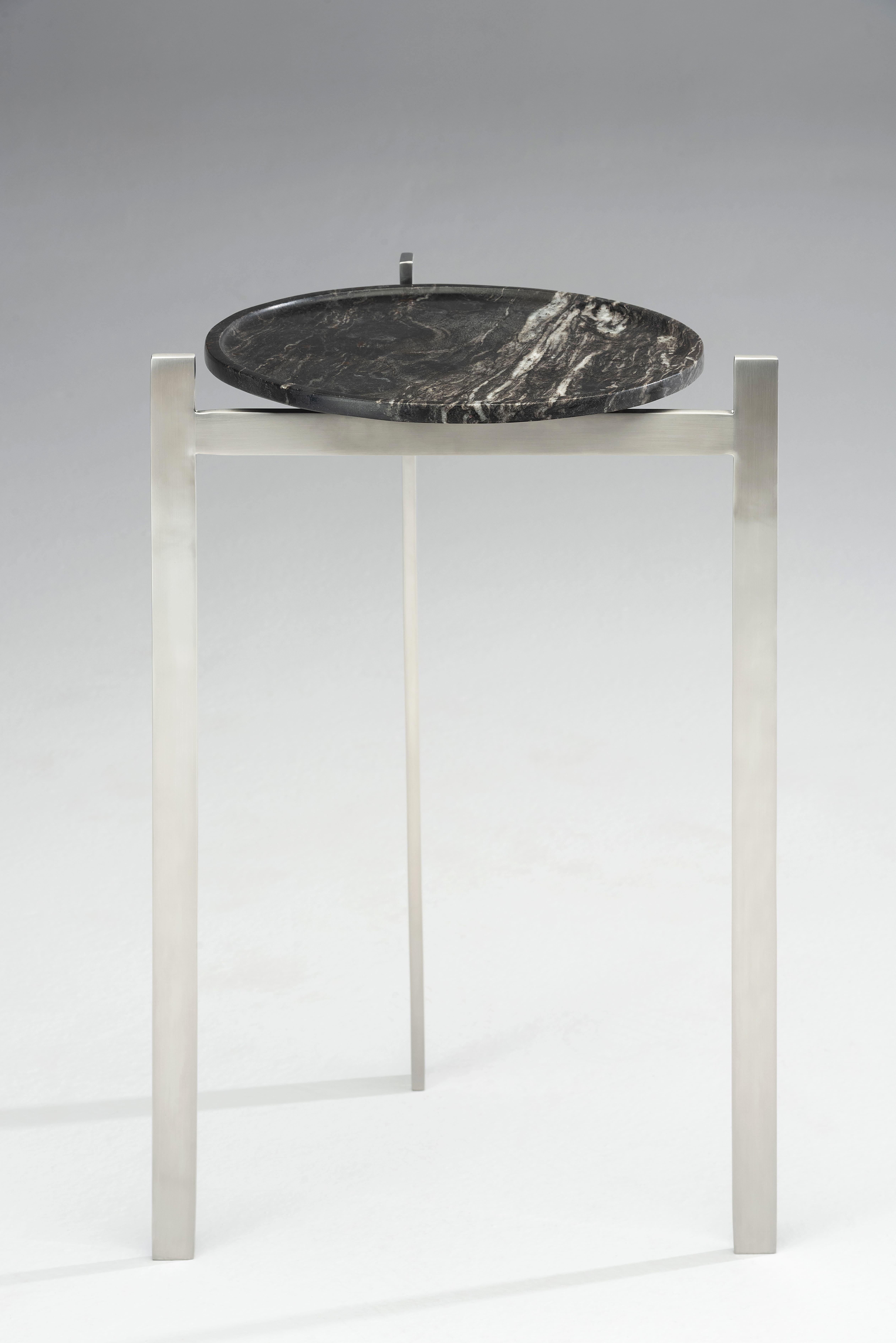 Der Disco Side Table von Zanini de Zanine ist ein eindrucksvolles Beispiel für die Fähigkeit des Designers, minimalistische Ästhetik mit industriellen Materialien zu verbinden. Der massive Sockel aus gebürstetem Edelstahl wird mit einer Steinplatte
