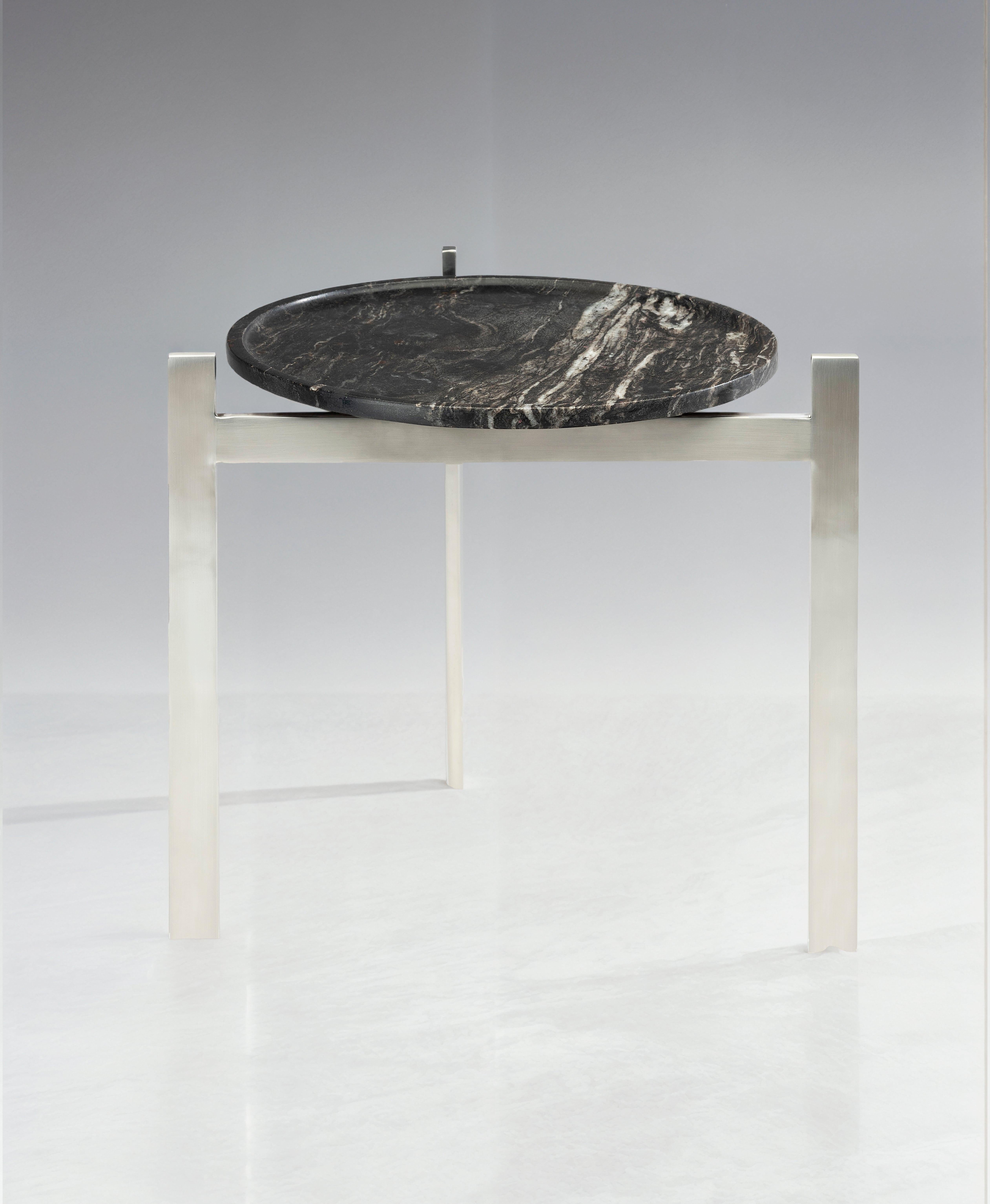 La Mesa auxiliar Disco de Zanini de Zanine es un ejemplo sorprendente de la habilidad del diseñador para combinar la estética minimalista con los materiales industriales. Presenta una sólida base de acero inoxidable cepillado combinada con una