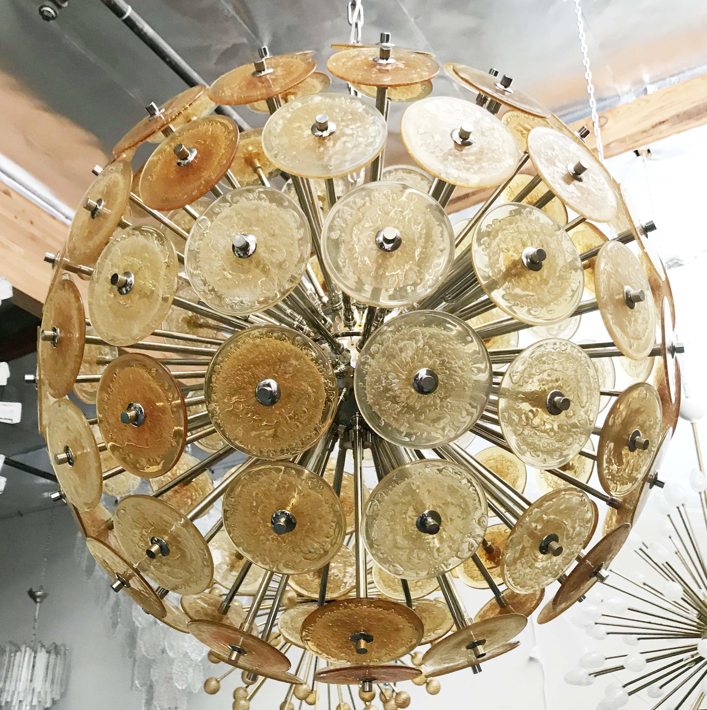 Lampadario italiano rotondo Sputnik con dischi in vetro di Murano ambrato soffiati a mano con bolle d'aria secondo la tecnica Pulegoso, montati su una struttura in metallo con finitura nichel, di Fabio Ltd, made in Italy
12 luci / tipo E12 o E14 /