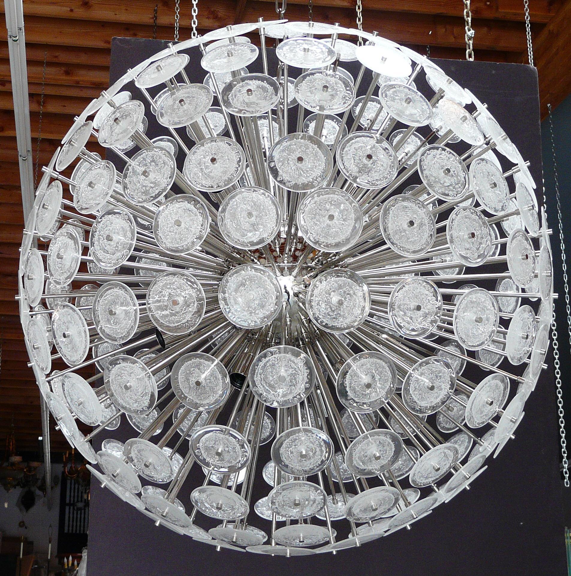 Araña sputnik redonda italiana con discos de cristal de Murano transparente soplado a mano con burbujas mediante la técnica Pulegoso, montada en estructura metálica con acabado niquelado por Fabio Ltd / Made in Italy
16 luces / tipo E26 o E27 / máx.